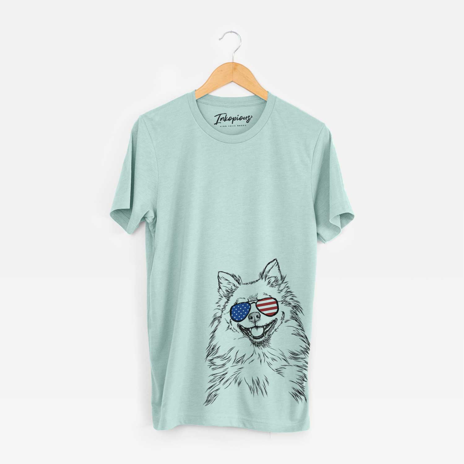 Hand-drawn sketch of Fibi the Spitz wearing American flag sunglasses on a Heather Sage Unisex crewneck