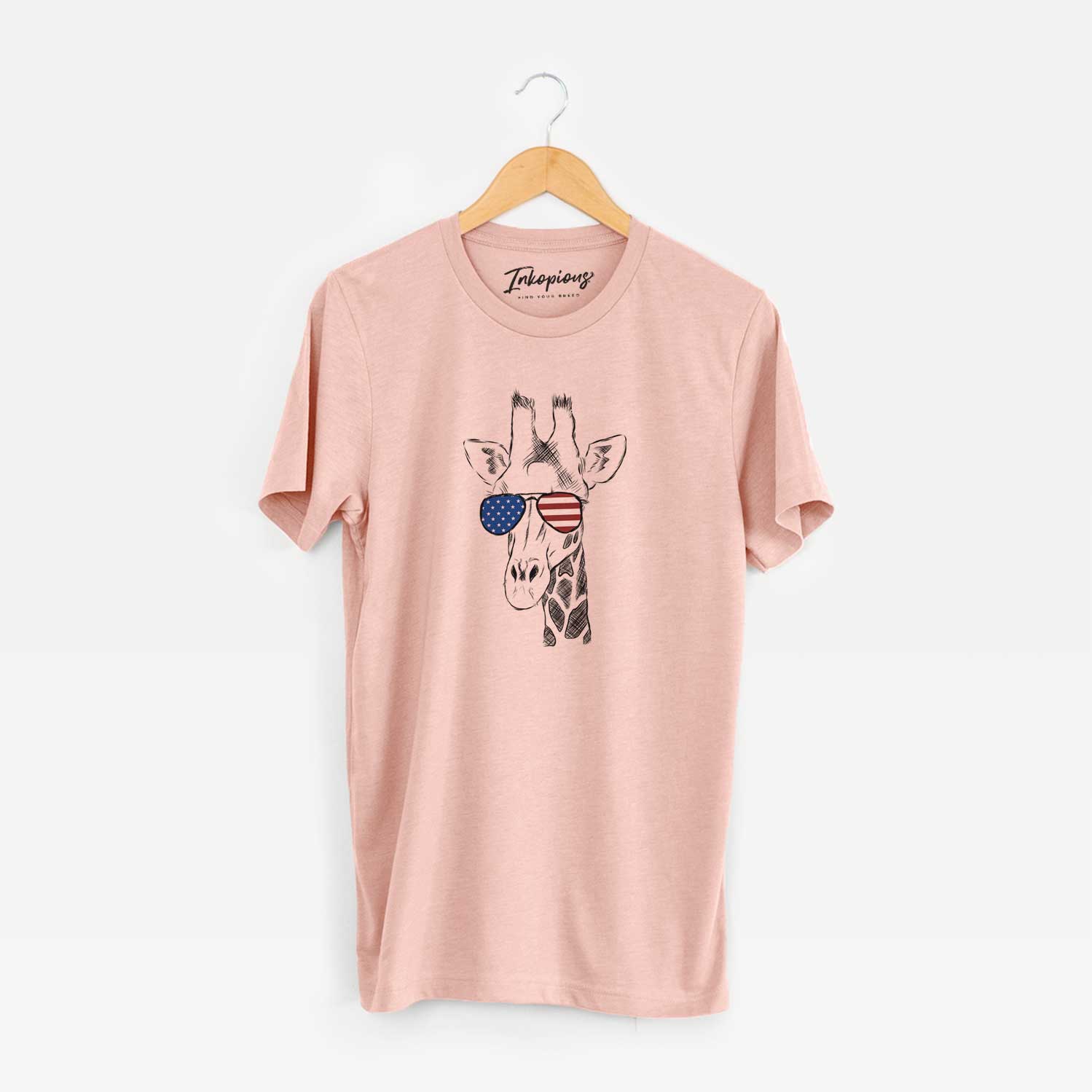 Hand-drawn sketch of Geoffrey the Giraffe wearing American flag sunglasses on a Peach Unisex crewneck