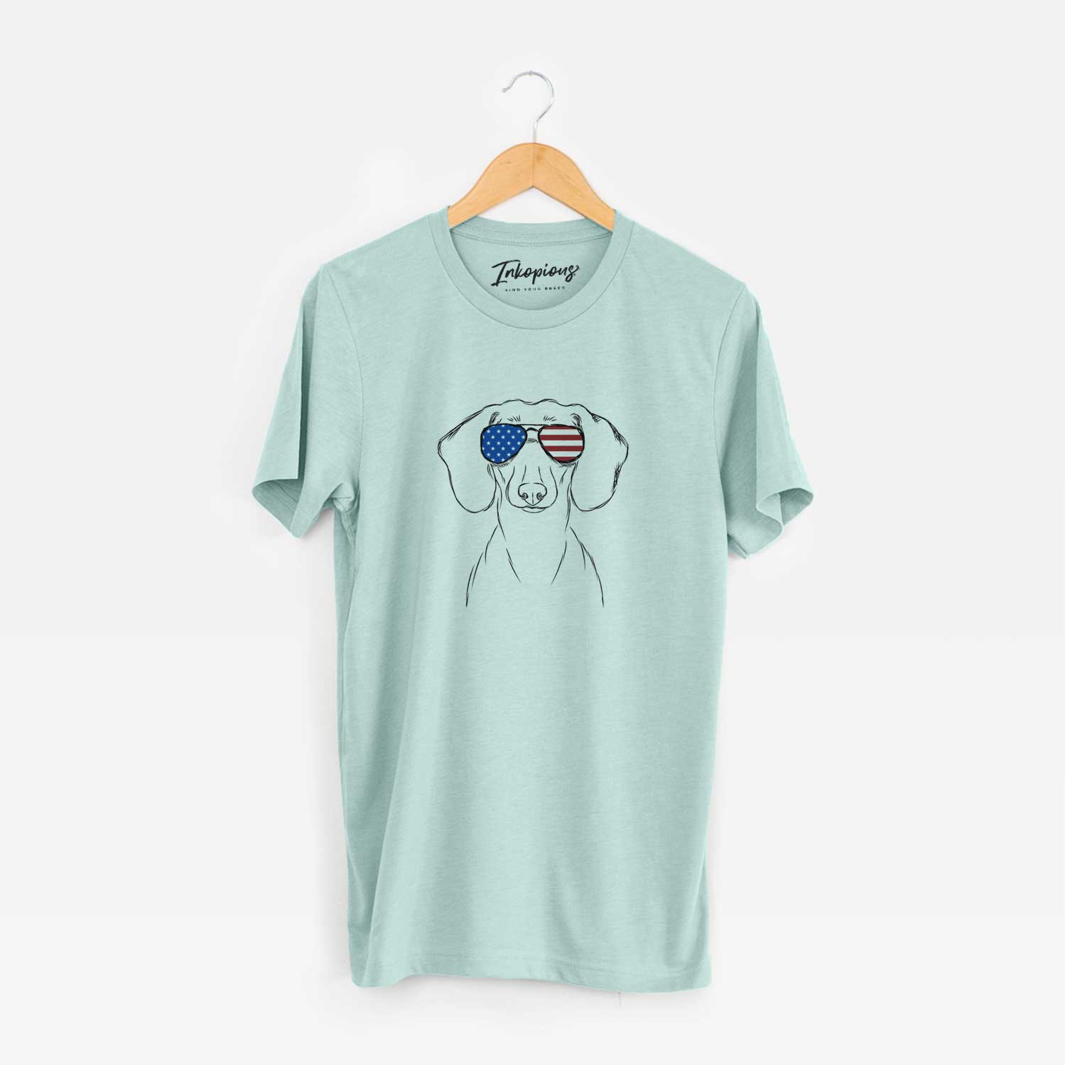 Hand-drawn sketch of Hans the Dachshund wearing American flag sunglasses on a Heather Sage Unisex crewneck