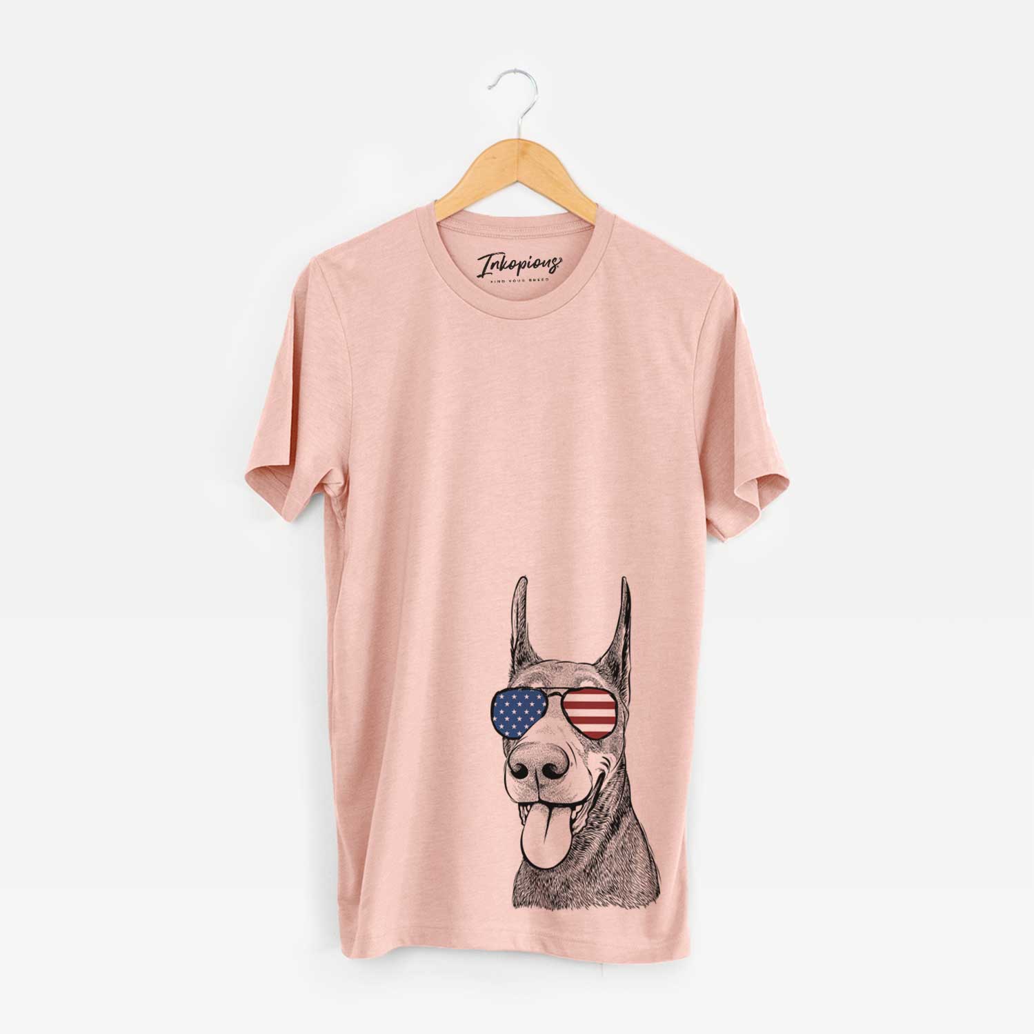 Hand-drawn sketch of Happy Sunny the Doberman Pinscher wearing American flag sunglasses on a Peach Unisex crewneck