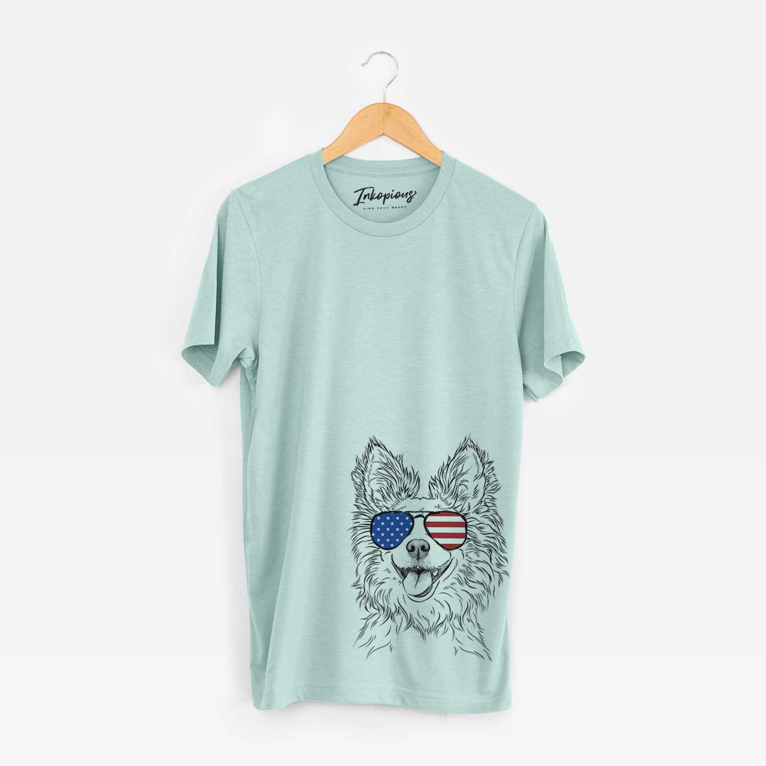 Hand-drawn sketch of Jasper the Pomchi wearing American flag sunglasses on a Heather Sage Unisex crewneck