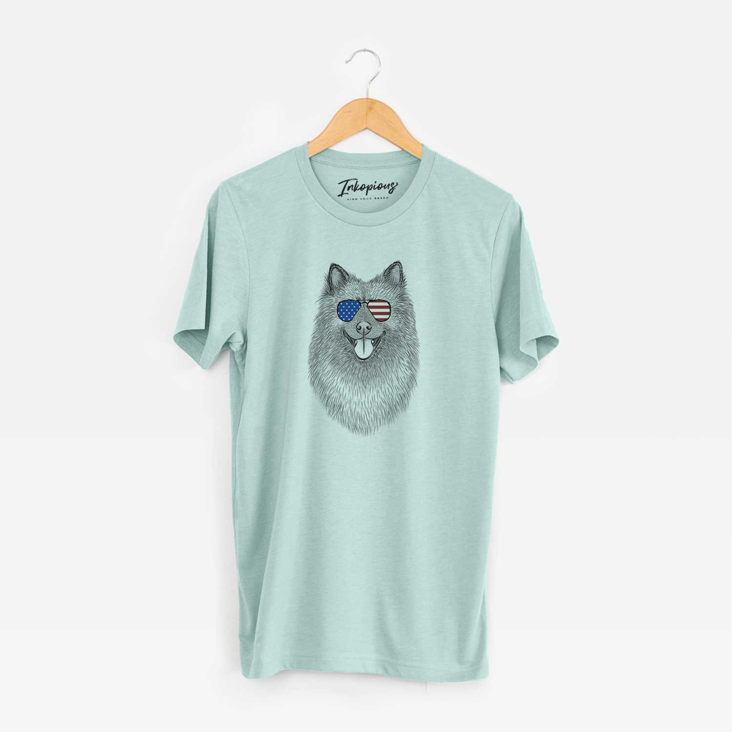 Hand-drawn sketch of Kai the Keeshond wearing American flag sunglasses on a Heather Sage Unisex crewneck