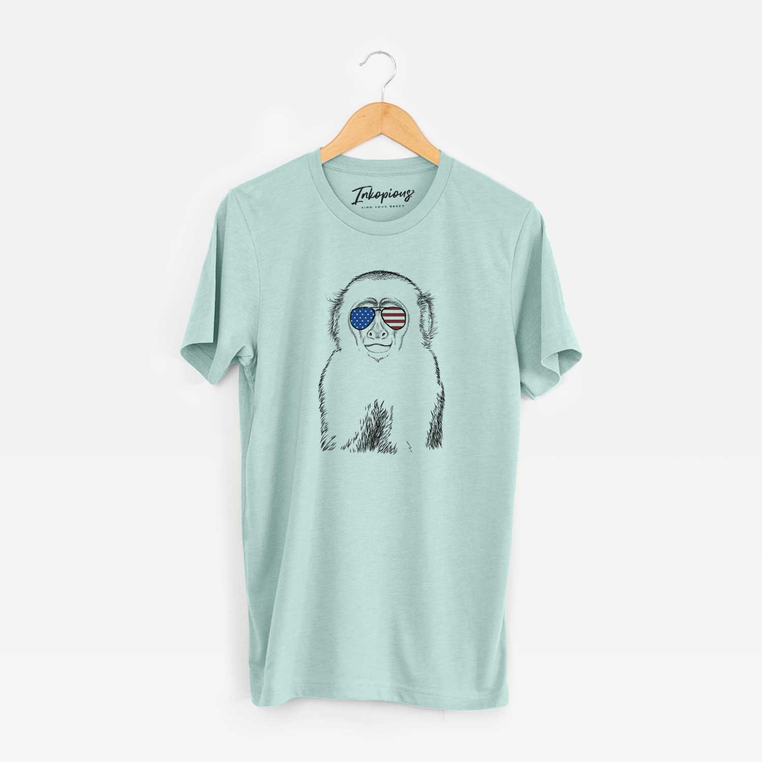 Hand-drawn sketch of Marcel the Capuchin Monkey wearing American flag sunglasses on a Heather Sage Unisex crewneck