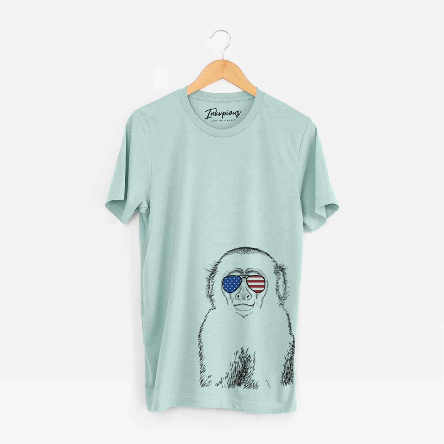 Hand-drawn sketch of Marcel the Capuchin Monkey wearing American flag sunglasses on a Heather Sage Unisex crewneck