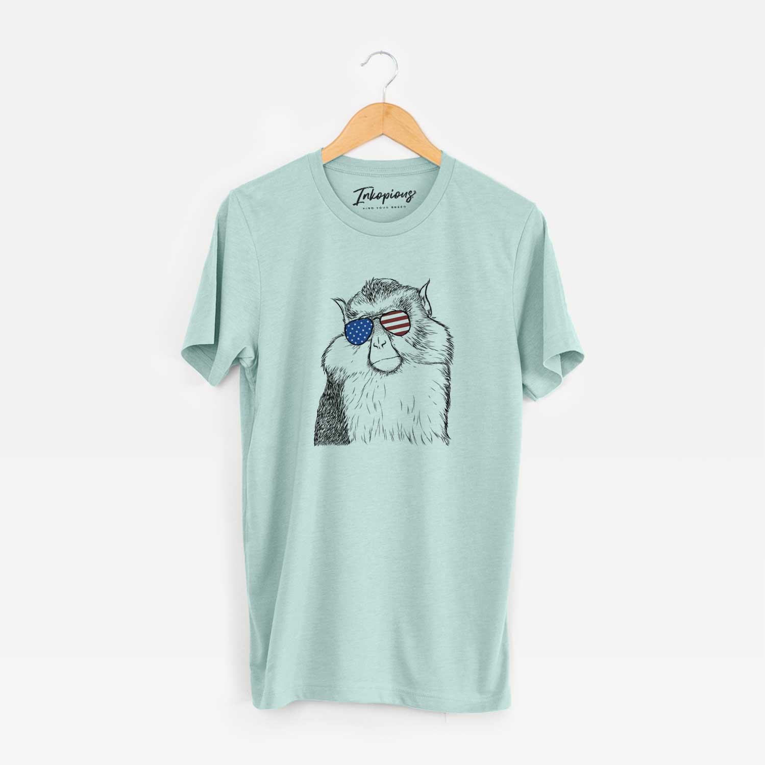 Hand-drawn sketch of Matata the Mona Monkey wearing American flag sunglasses on a Heather Sage Unisex crewneck