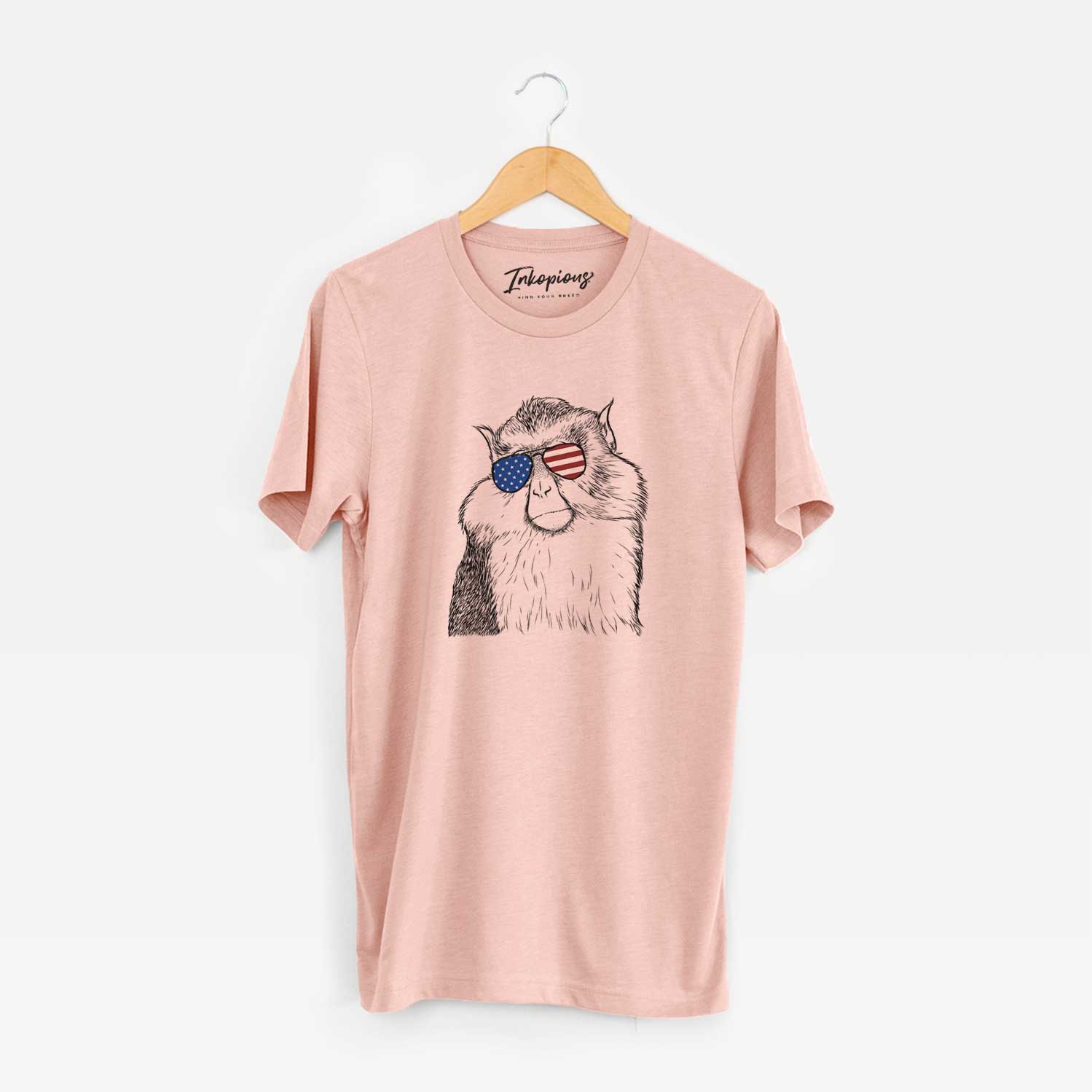 Hand-drawn sketch of Matata the Mona Monkey wearing American flag sunglasses on a Peach Unisex crewneck