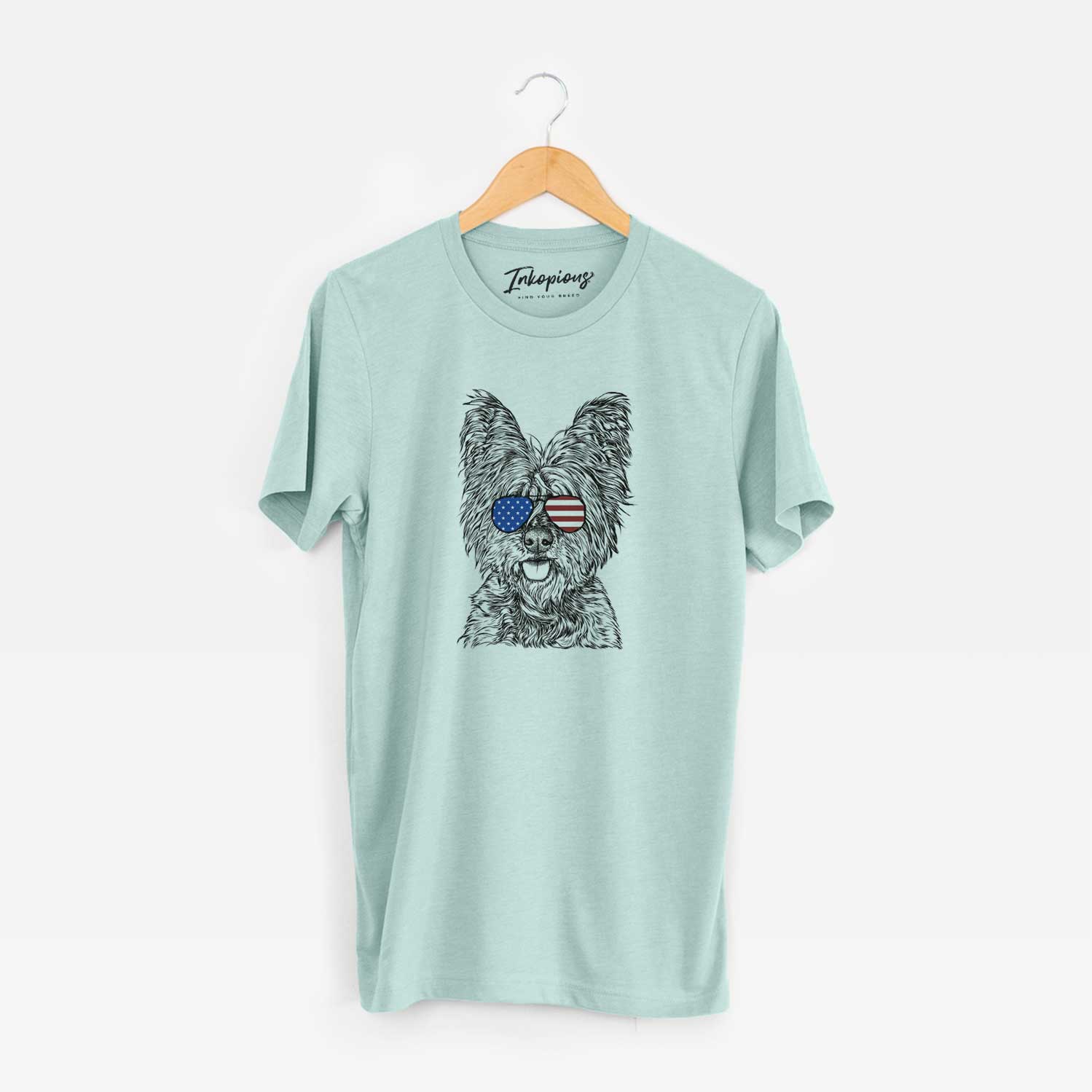 Hand-drawn sketch of McDuff the Cairn Terrier wearing American flag sunglasses on a Heather Sage Unisex crewneck