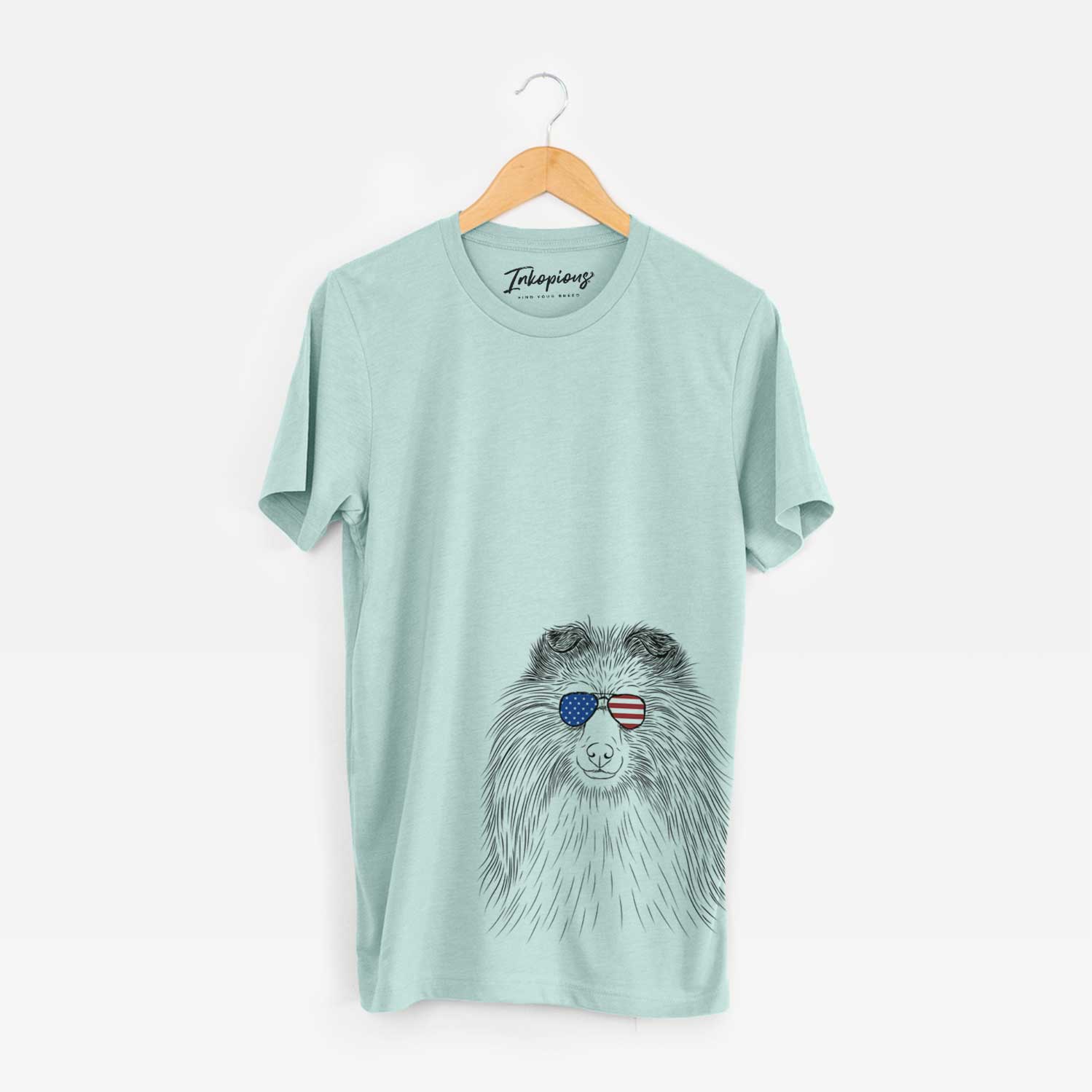 Hand-drawn sketch of Moxie the Shetland Sheepdog wearing American flag sunglasses on a Heather Sage Unisex crewneck