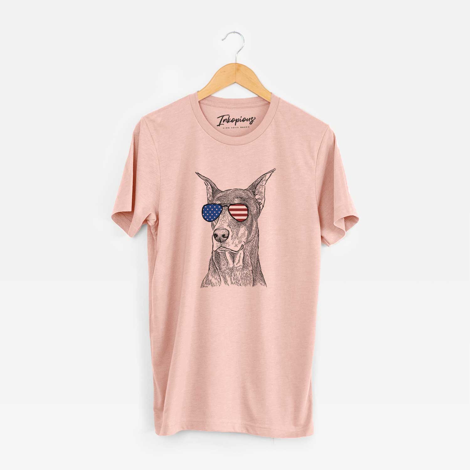 Hand-drawn sketch of RJ the Doberman Pinscher wearing American flag sunglasses on a Peach Unisex crewneck