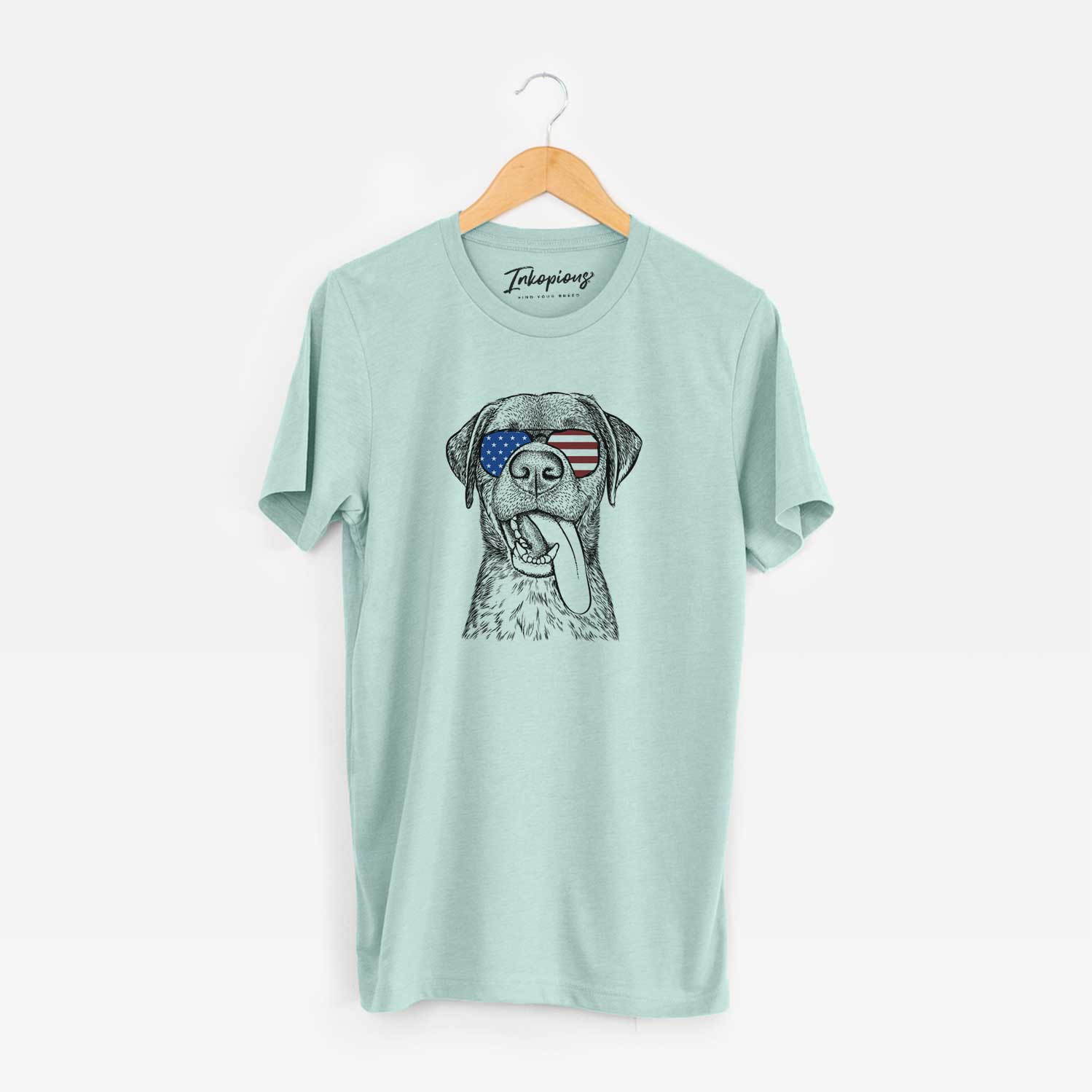 Hand-drawn sketch of Reese the Mixed Breed wearing American flag sunglasses on a Heather Sage Unisex crewneck
