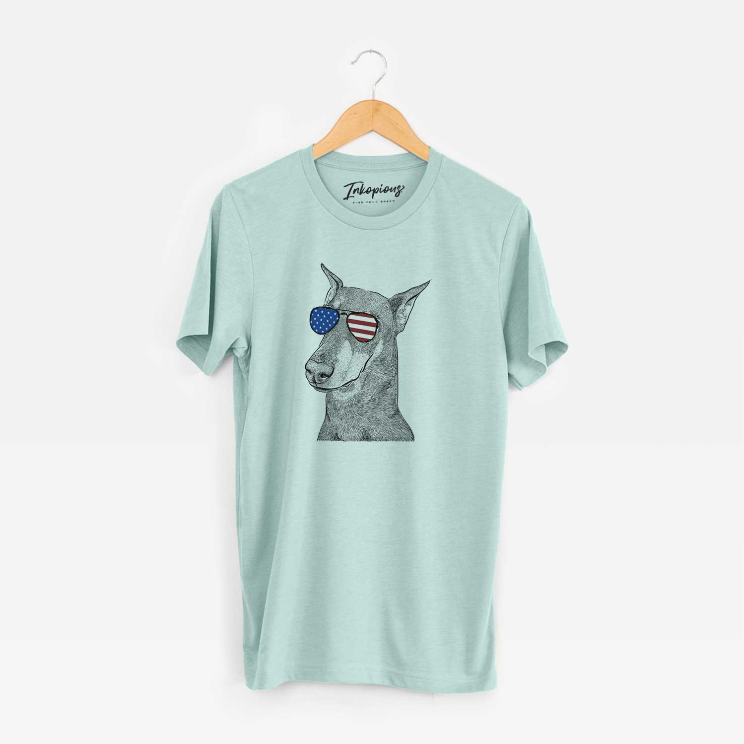 Hand-drawn sketch of Shelby the Doberman Pinscher wearing American flag sunglasses on a Heather Sage Unisex crewneck