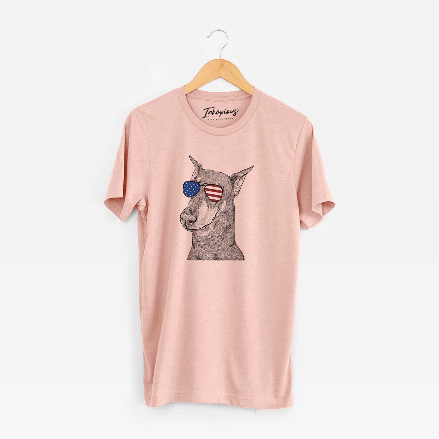 Hand-drawn sketch of Shelby the Doberman Pinscher wearing American flag sunglasses on a Peach Unisex crewneck