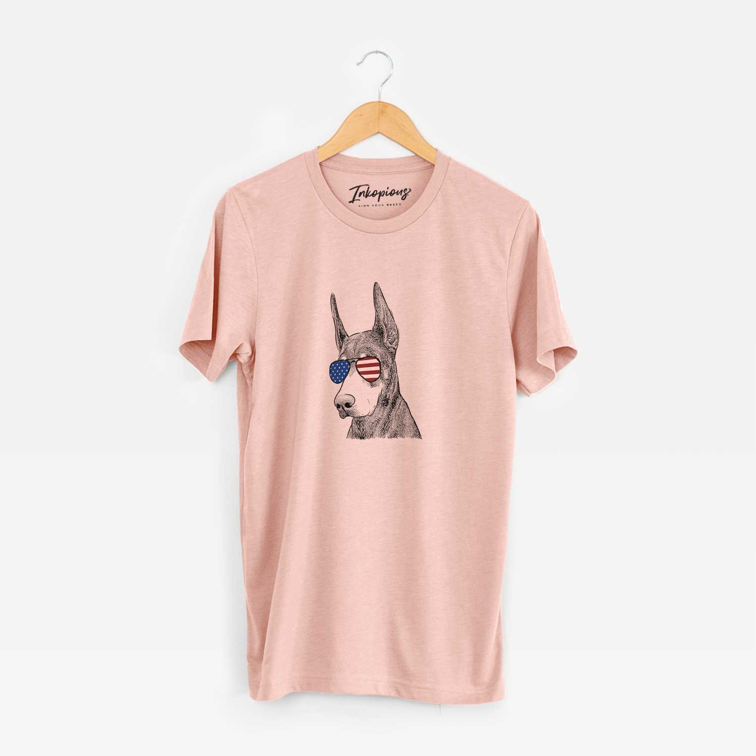 Hand-drawn sketch of Sunny the Doberman Pinscher wearing American flag sunglasses on a Peach Unisex crewneck