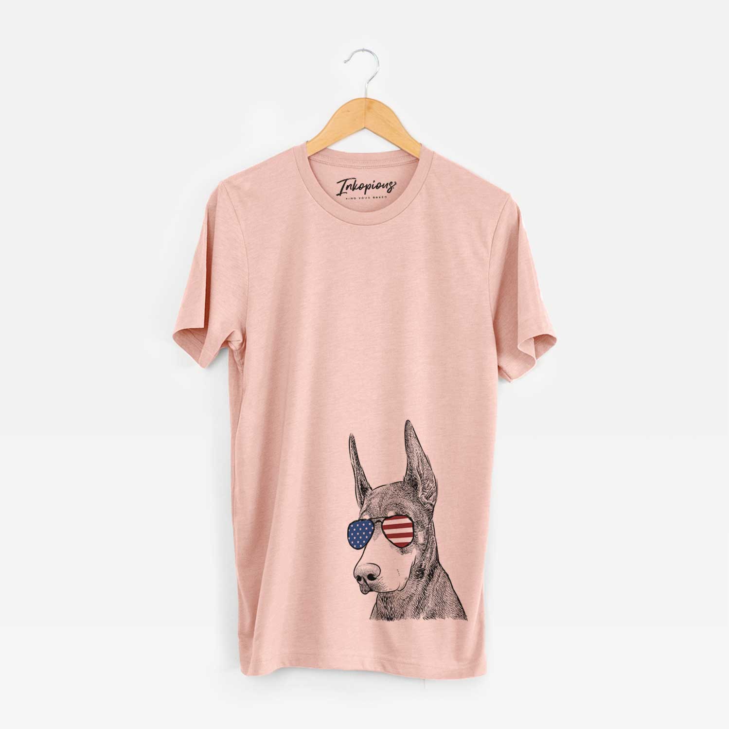 Hand-drawn sketch of Sunny the Doberman Pinscher wearing American flag sunglasses on a Peach Unisex crewneck