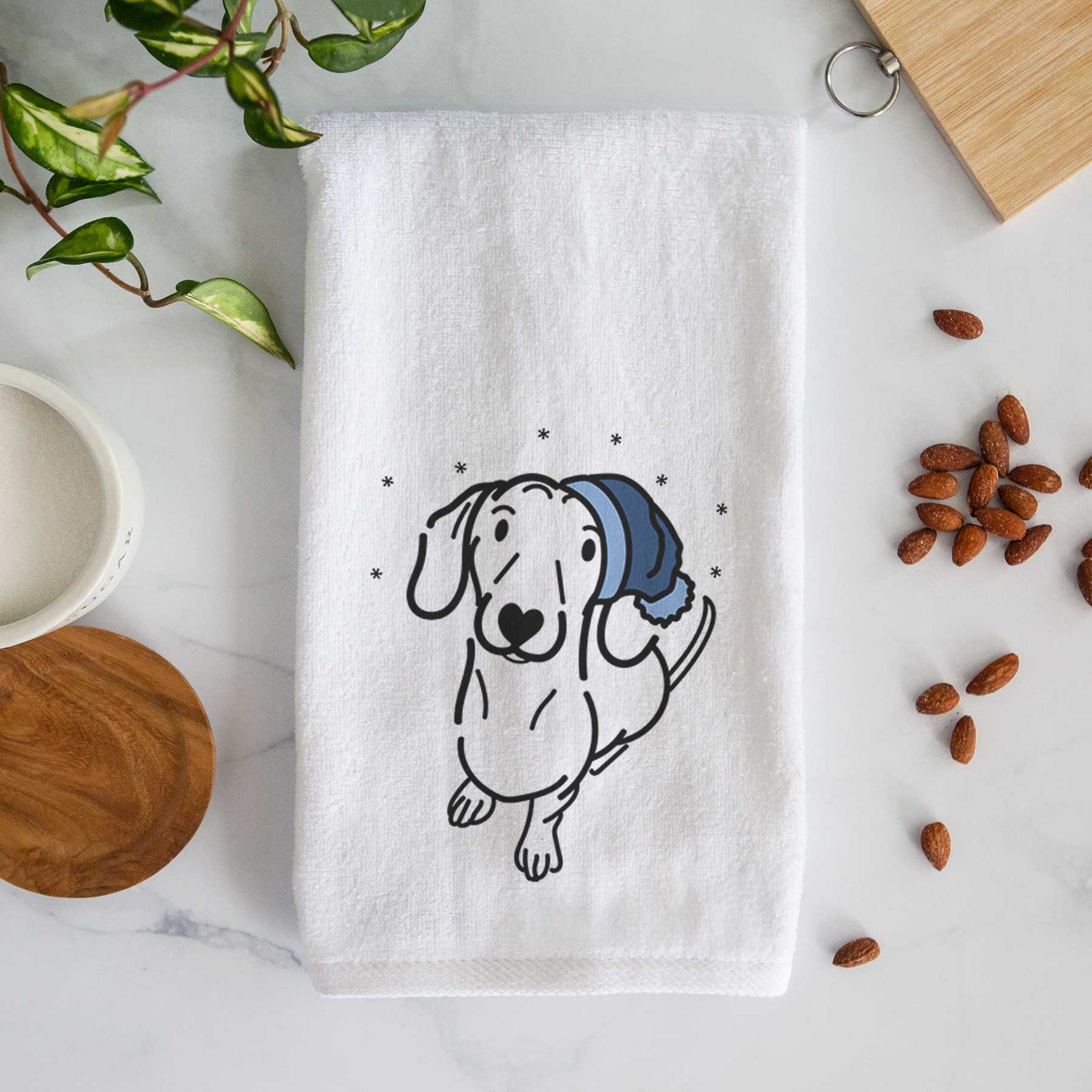 Minimalist line drawing of Moxie the Dachshund wearing a winter beanie on a decorative hand towel