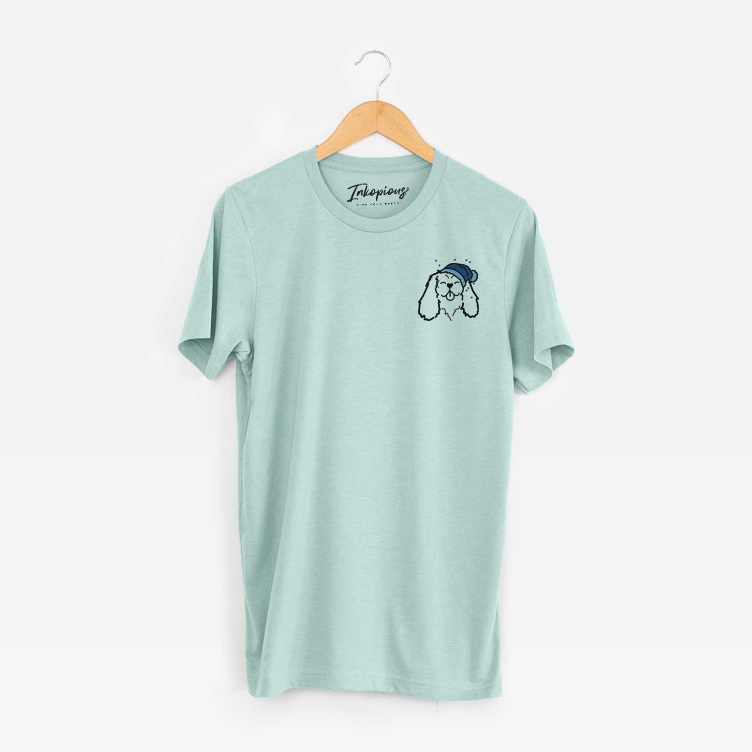 Small chest-pocket minimalist line drawing of a Cavalier King Charles Spaniel wearing a winter beanie on a Heather Sage Unisex crewneck