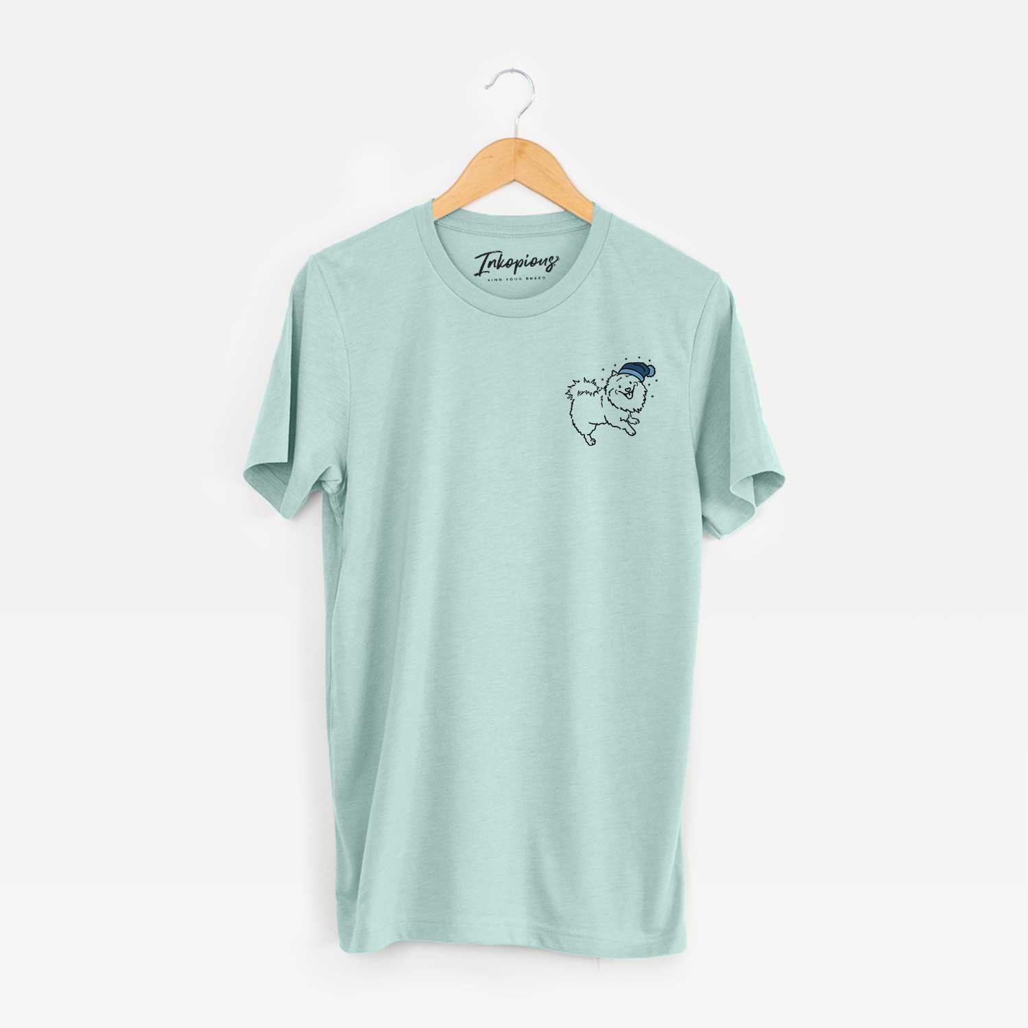 Small chest-pocket minimalist line drawing of Goldie the Pomeranian Mix wearing a winter beanie on a Heather Sage Unisex crewneck