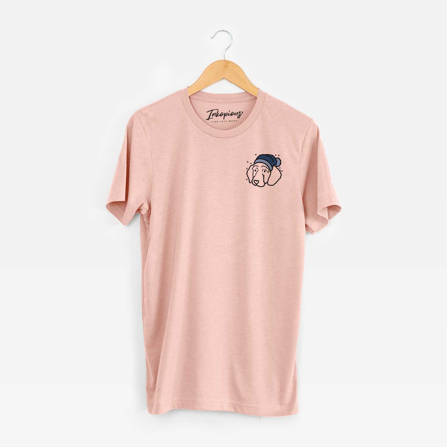Small chest-pocket minimalist line drawing of Hanna the Goldendoodle wearing a winter beanie on a Peach Unisex crewneck