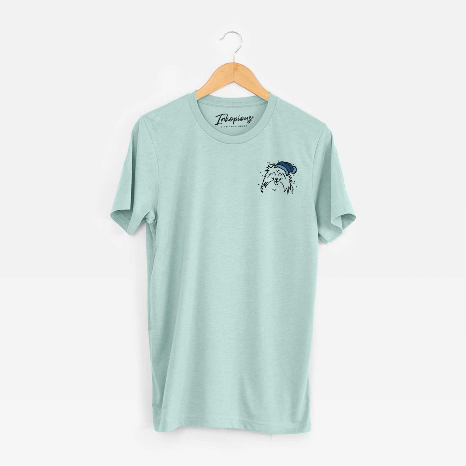 Small chest-pocket minimalist line drawing of a Rough Collie wearing a winter beanie on a Heather Sage Unisex crewneck