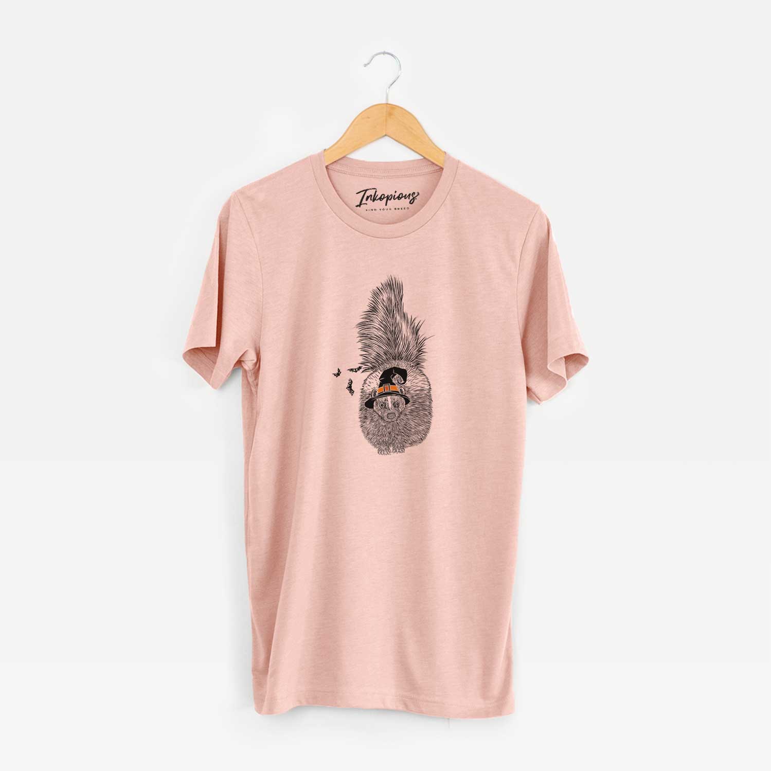Hand-drawn sketch of Tibbs the Skunk wearing a witch hat on a Peach Unisex crewneck