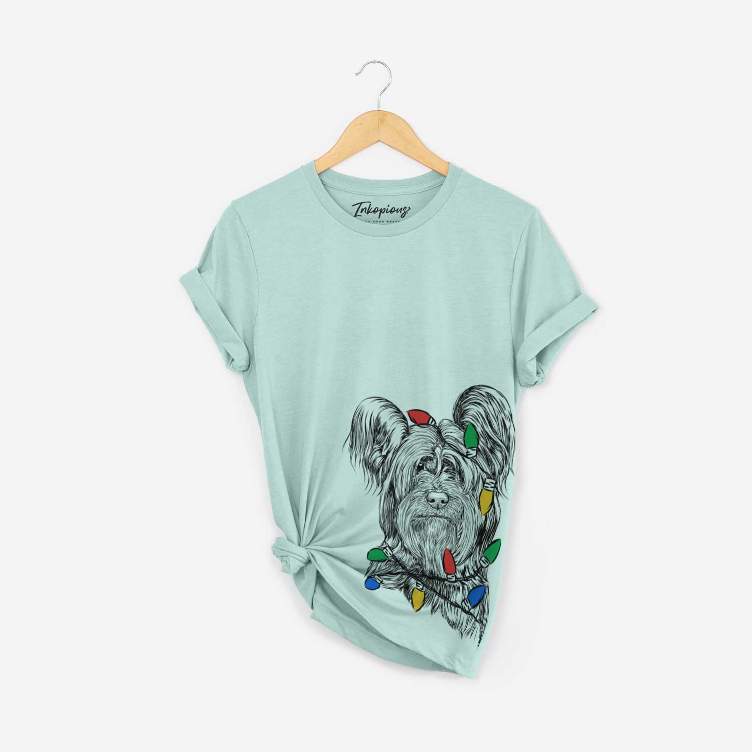 Hand-drawn sketch of Bandit the Skye Terrier wrapped in Christmas lights on a Heather Sage Unisex crewneck