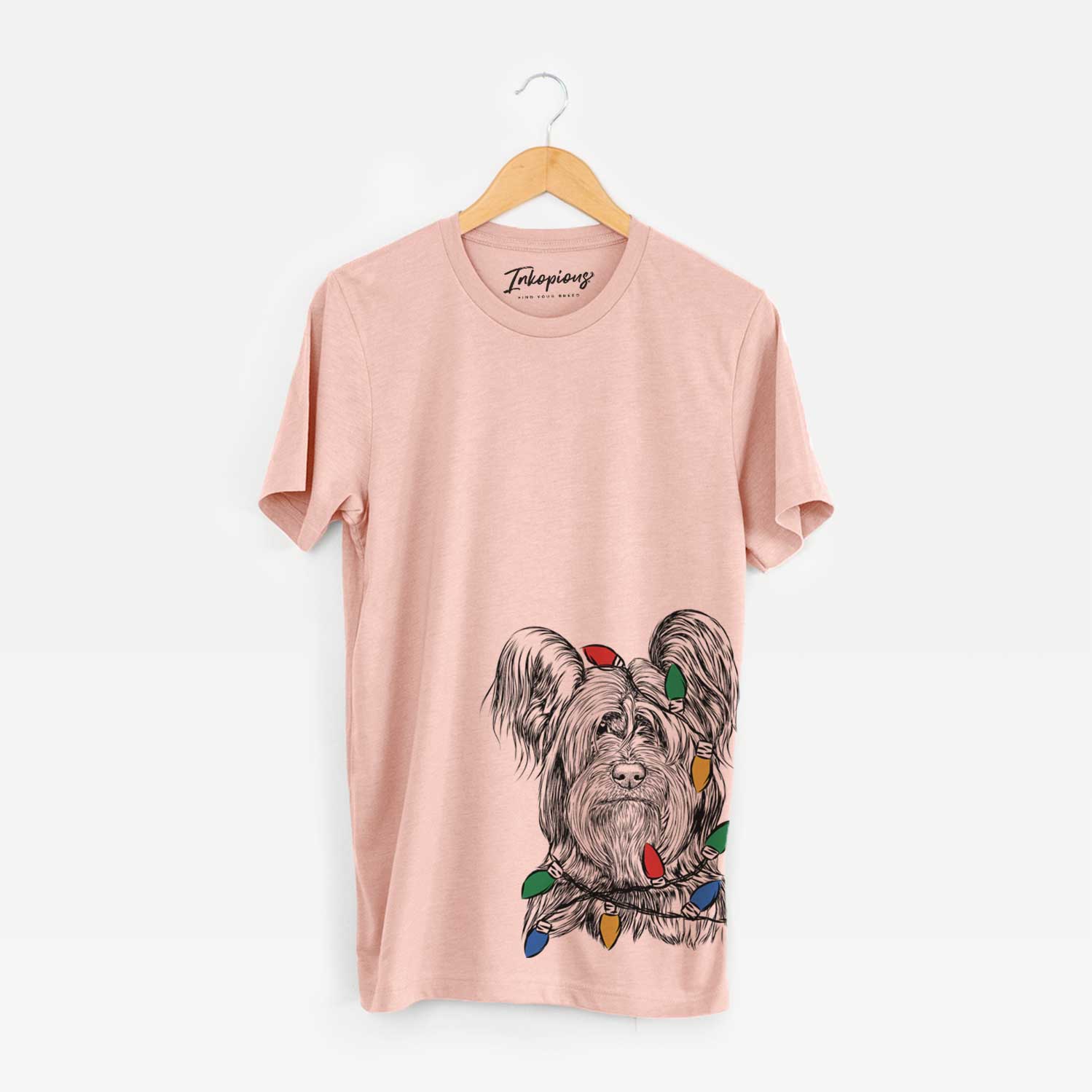 Hand-drawn sketch of Bandit the Skye Terrier wrapped in Christmas lights on a Peach Unisex crewneck