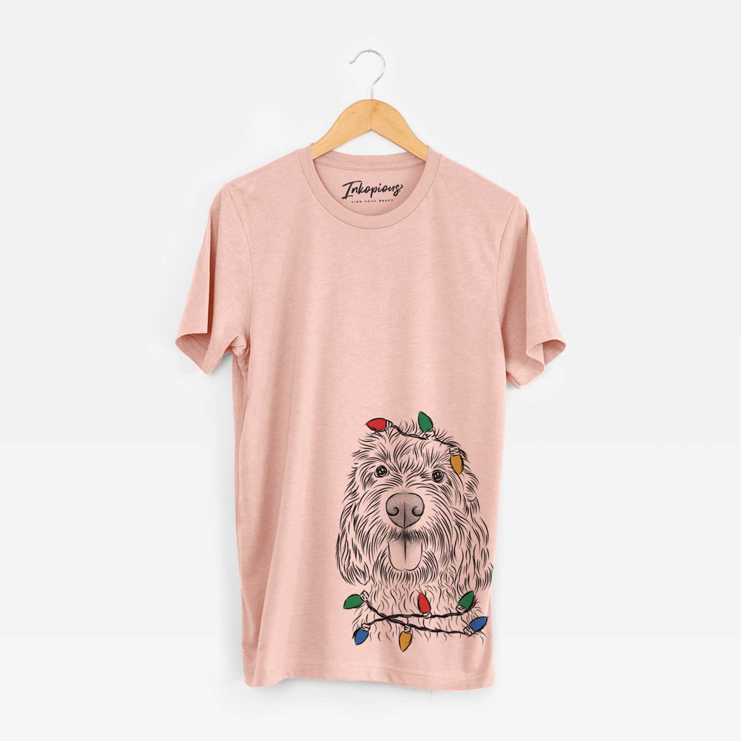Hand-drawn sketch of Clover the Cockapoo wrapped in Christmas lights on a Peach Unisex crewneck