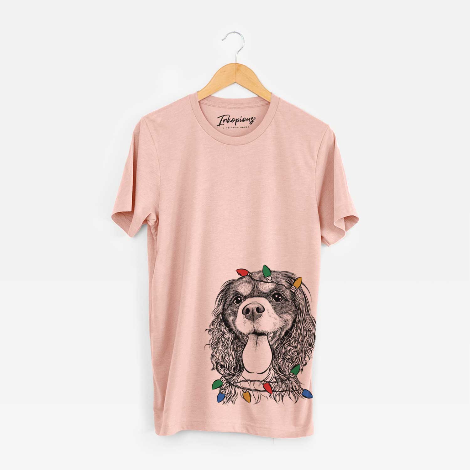 Hand-drawn sketch of Elizabeth the Cavalier King Charles Spaniel wrapped in Christmas lights on a Peach Unisex crewneck