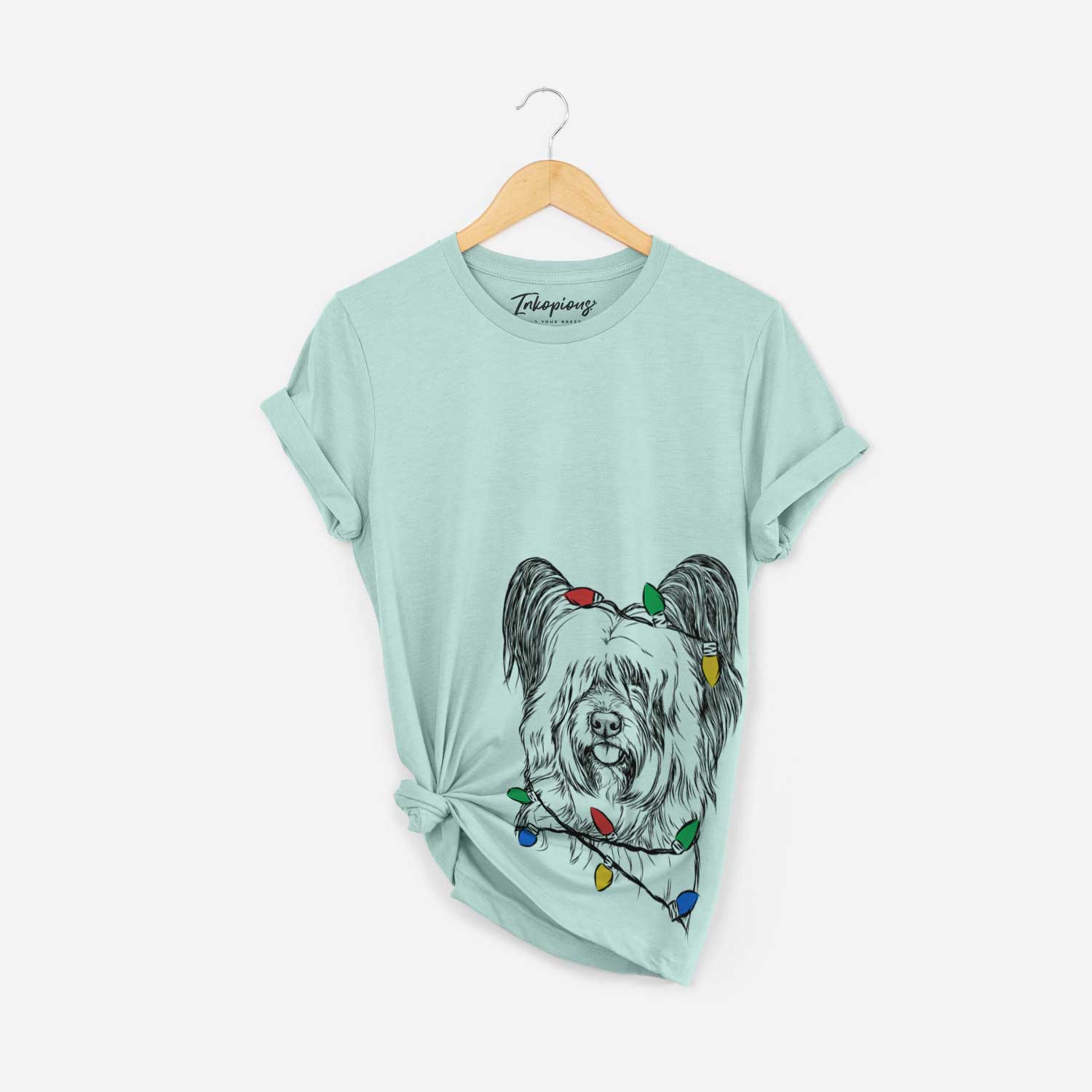 Hand-drawn sketch of Gideon the Skye Terrier wrapped in Christmas lights on a Heather Sage Unisex crewneck