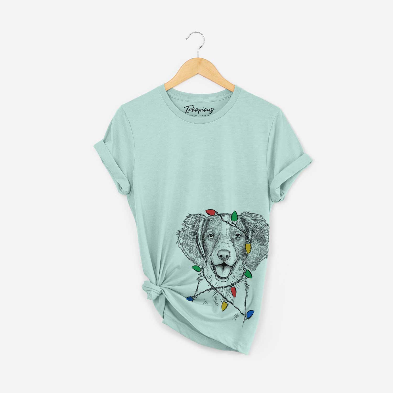 Hand-drawn sketch of Happy Holly the Brittany Spaniel wrapped in Christmas lights on a Heather Sage Unisex crewneck