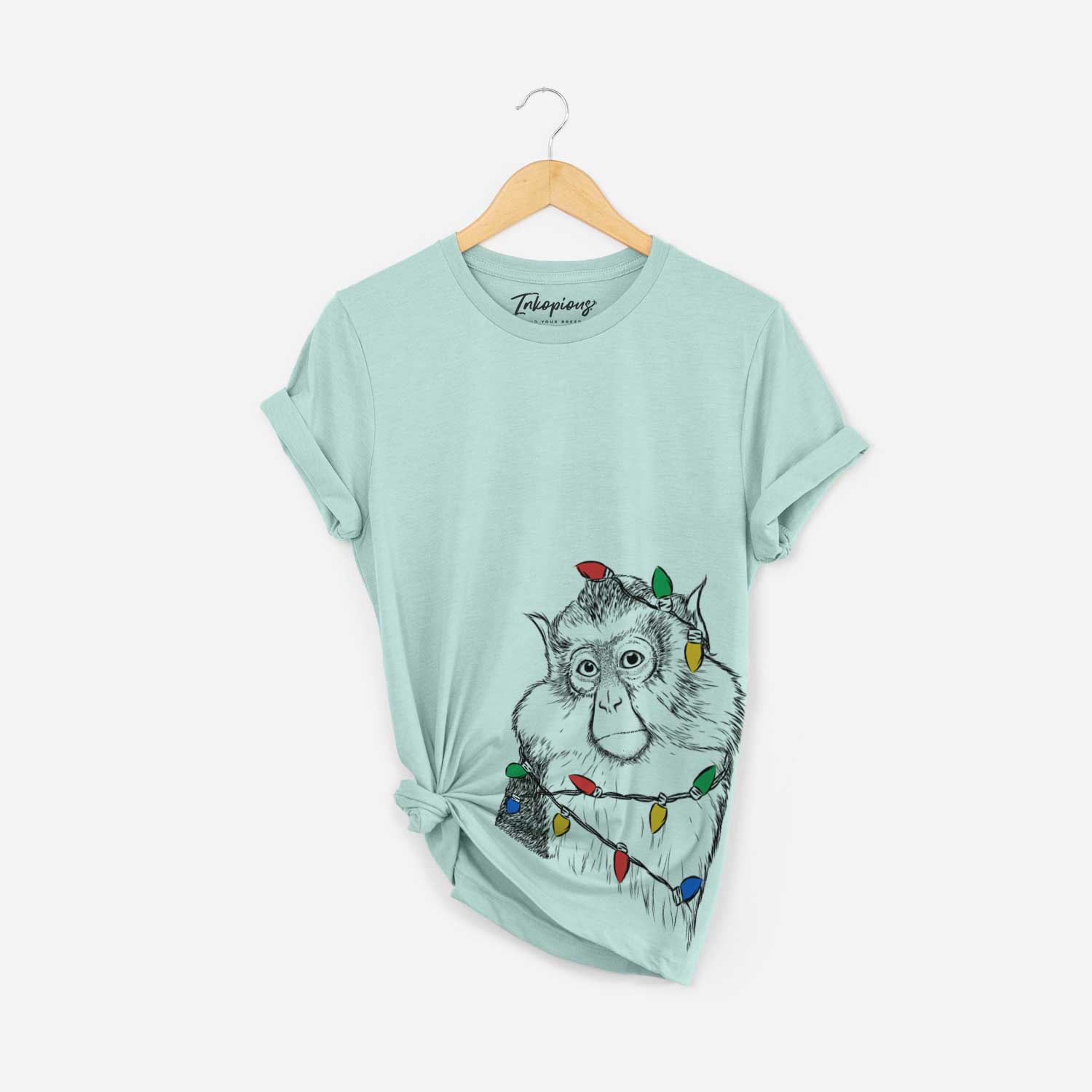 Hand-drawn sketch of Matata the Mona Monkey wrapped in Christmas lights on a Heather Sage Unisex crewneck