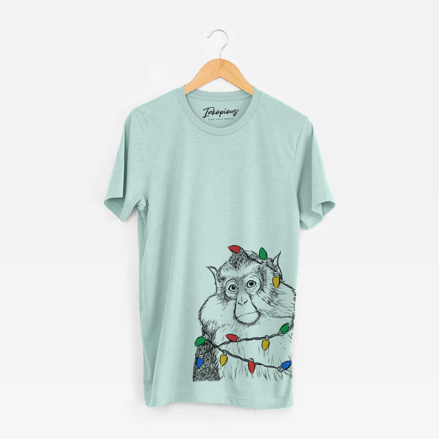 Hand-drawn sketch of Matata the Mona Monkey wrapped in Christmas lights on a Heather Sage Unisex crewneck