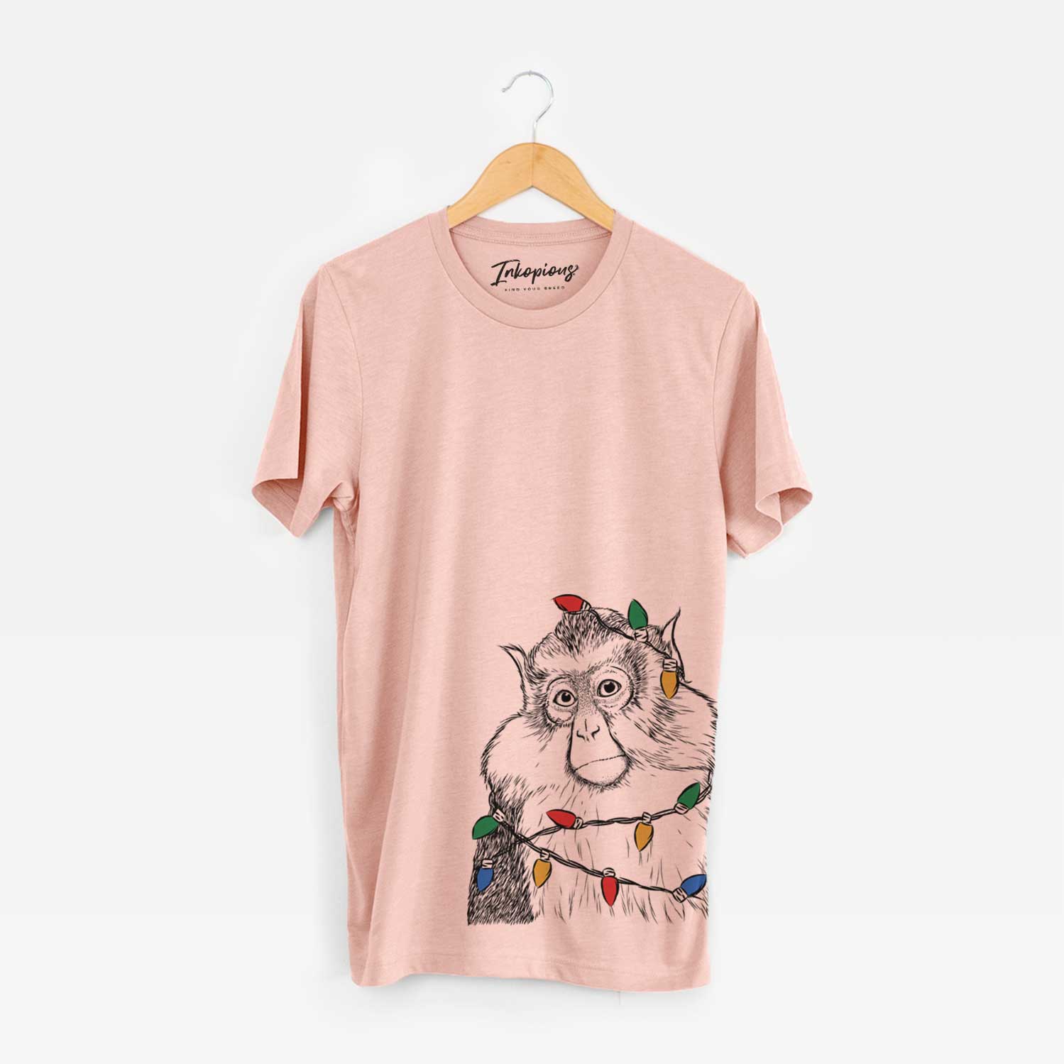 Hand-drawn sketch of Matata the Mona Monkey wrapped in Christmas lights on a Peach Unisex crewneck