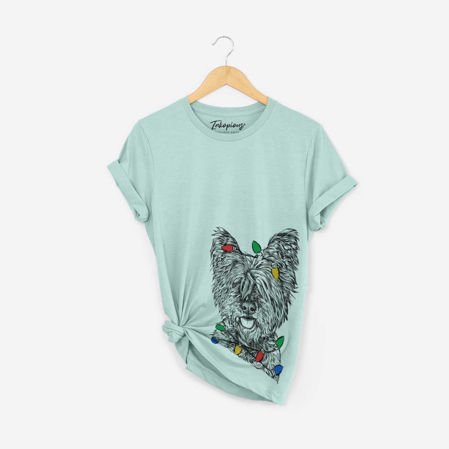 Hand-drawn sketch of McDuff the Cairn Terrier wrapped in Christmas lights on a Heather Sage Unisex crewneck