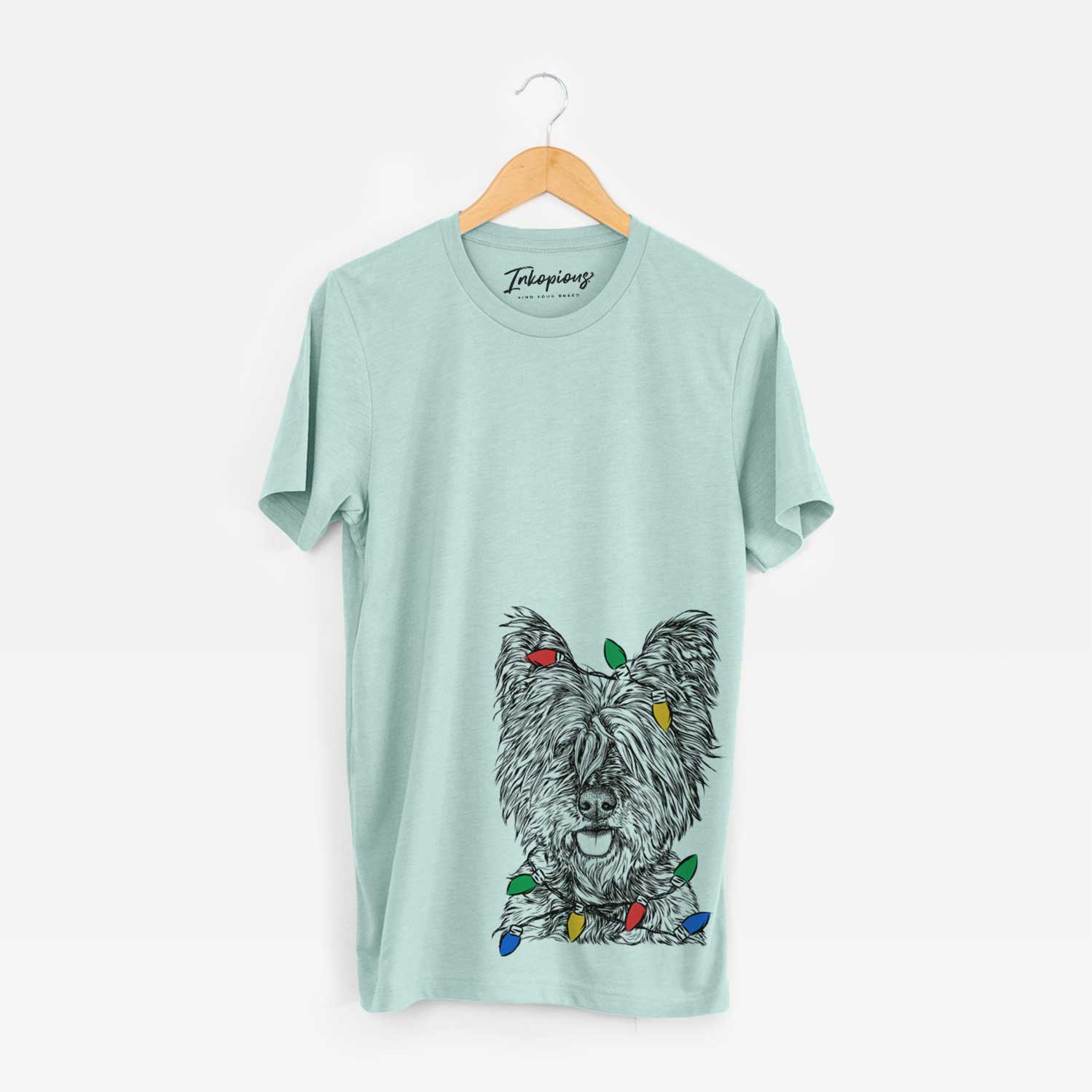 Hand-drawn sketch of McDuff the Cairn Terrier wrapped in Christmas lights on a Heather Sage Unisex crewneck