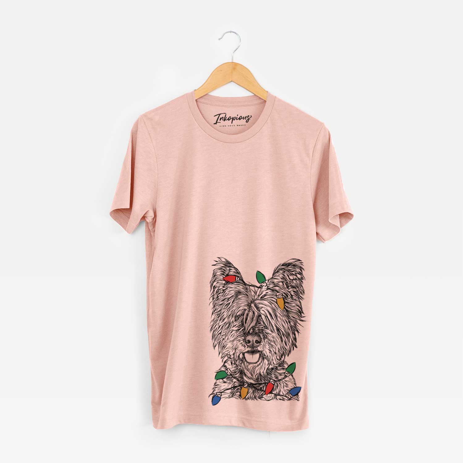 Hand-drawn sketch of McDuff the Cairn Terrier wrapped in Christmas lights on a Peach Unisex crewneck
