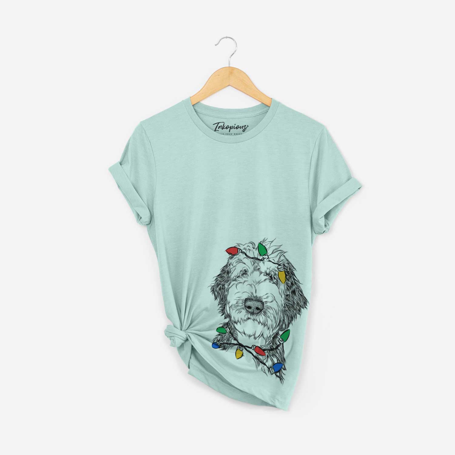 Hand-drawn sketch of Milo Fluff the Sheepadoodle wrapped in Christmas lights on a Heather Sage Unisex crewneck