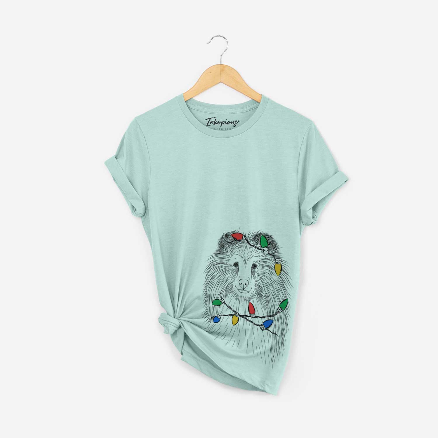 Hand-drawn sketch of Moxie the Shetland Sheepdog wrapped in Christmas lights on a Heather Sage Unisex crewneck
