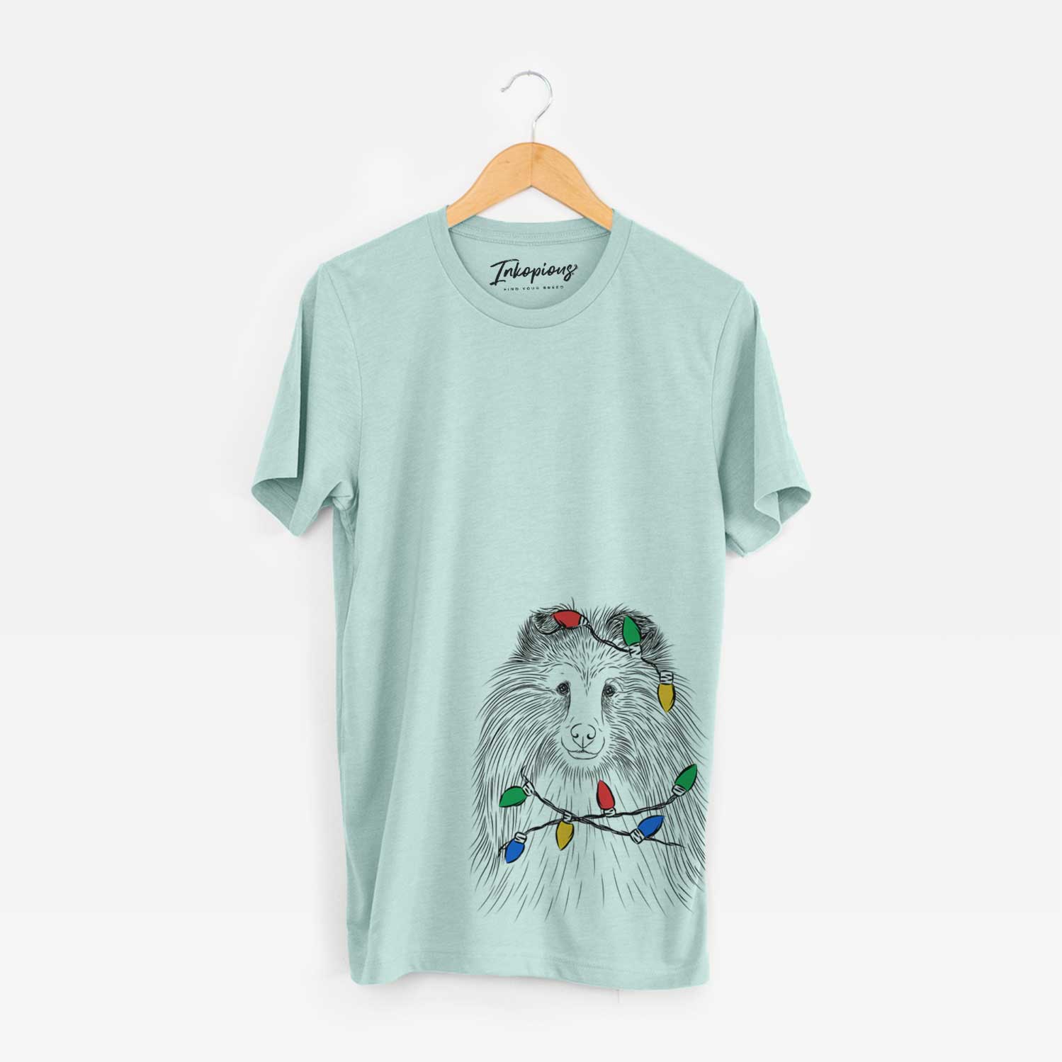 Hand-drawn sketch of Moxie the Shetland Sheepdog wrapped in Christmas lights on a Heather Sage Unisex crewneck