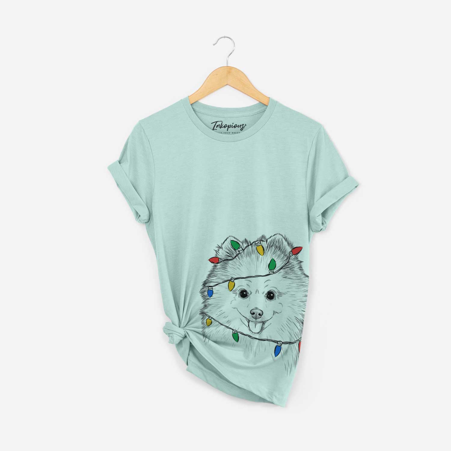 Hand-drawn sketch of Piper Jo the Pomeranian wrapped in Christmas lights on a Heather Sage Unisex crewneck