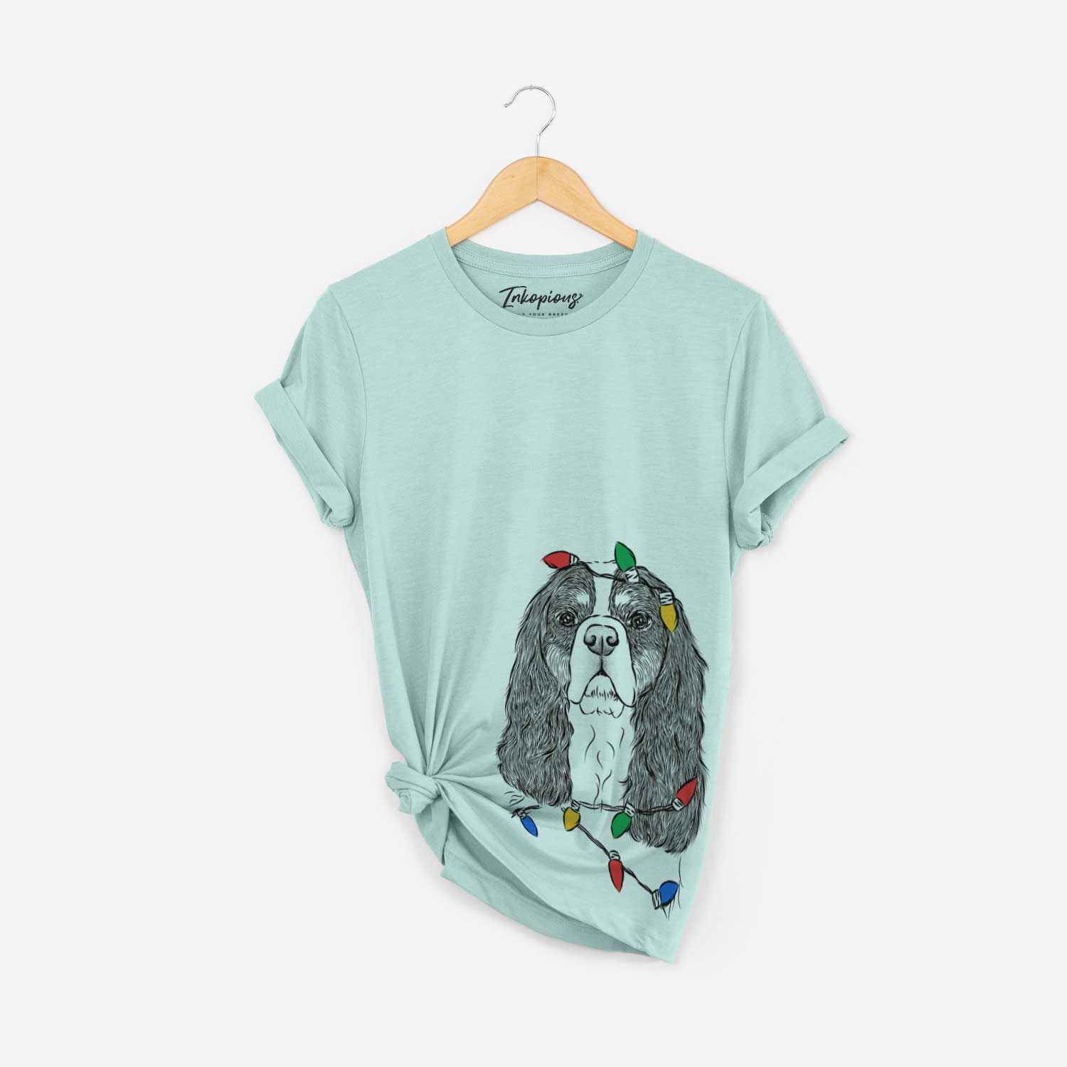Hand-drawn sketch of Sebastian the Cavalier King Charles Spaniel wrapped in Christmas lights on a Heather Sage Unisex crewneck