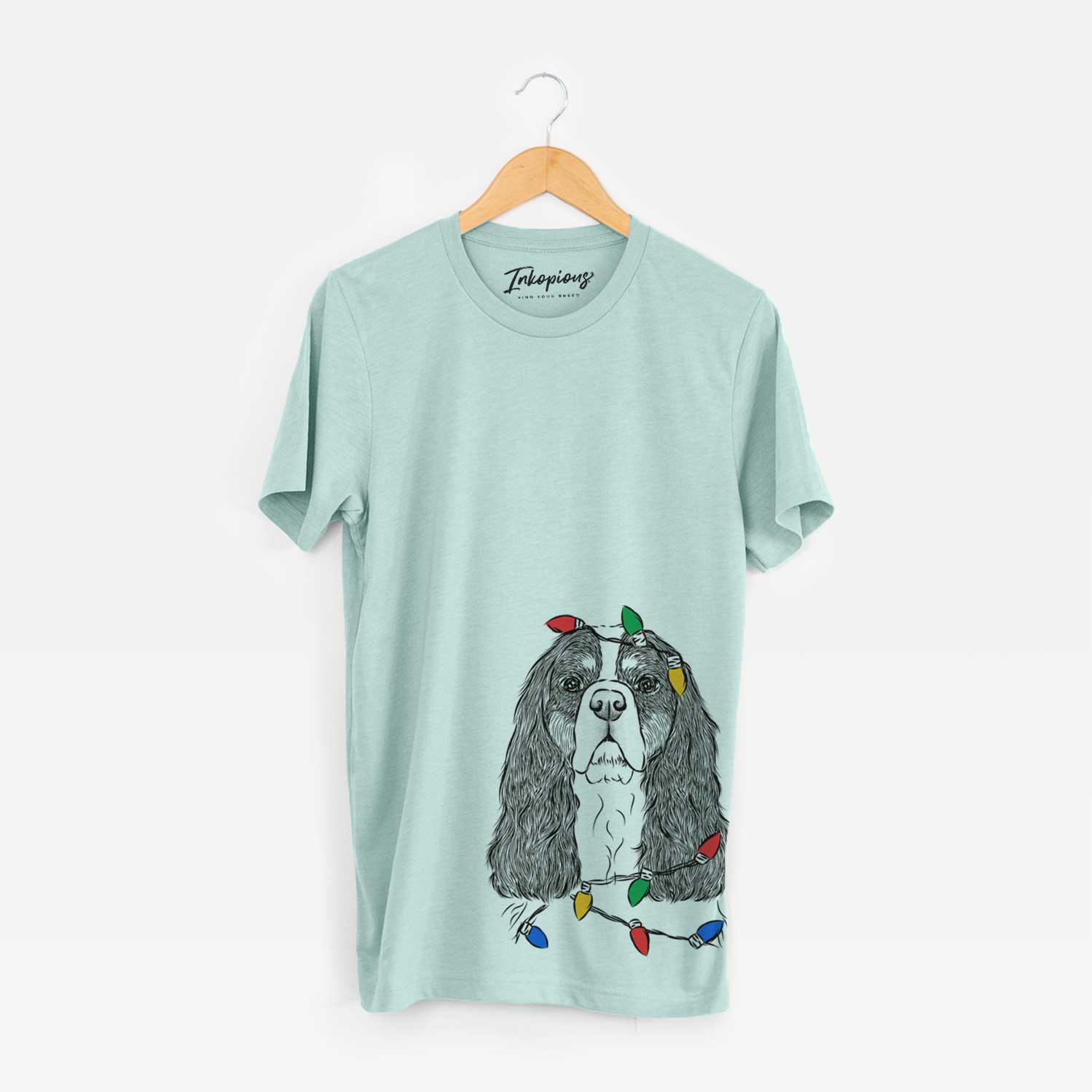Hand-drawn sketch of Sebastian the Cavalier King Charles Spaniel wrapped in Christmas lights on a Heather Sage Unisex crewneck