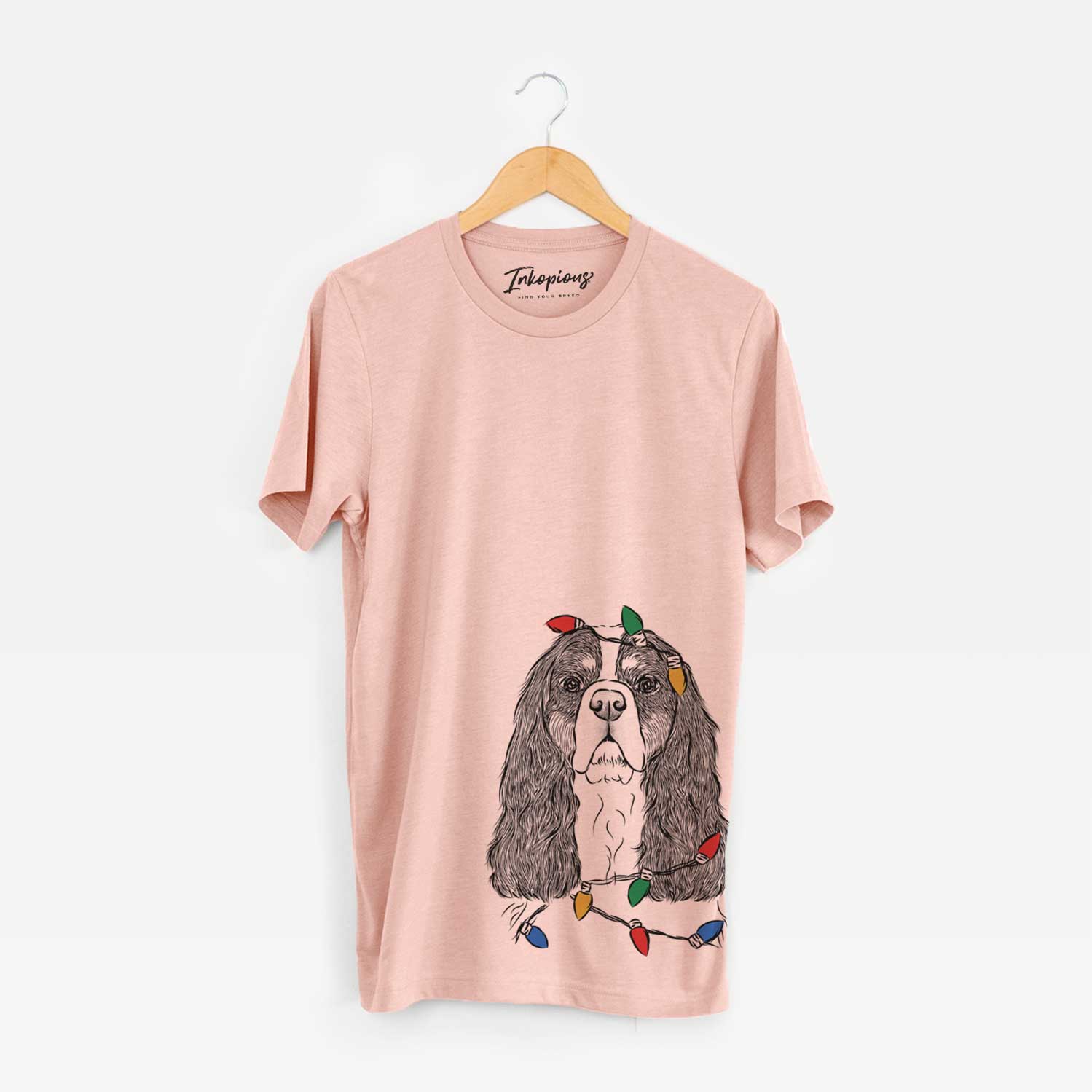 Hand-drawn sketch of Sebastian the Cavalier King Charles Spaniel wrapped in Christmas lights on a Peach Unisex crewneck