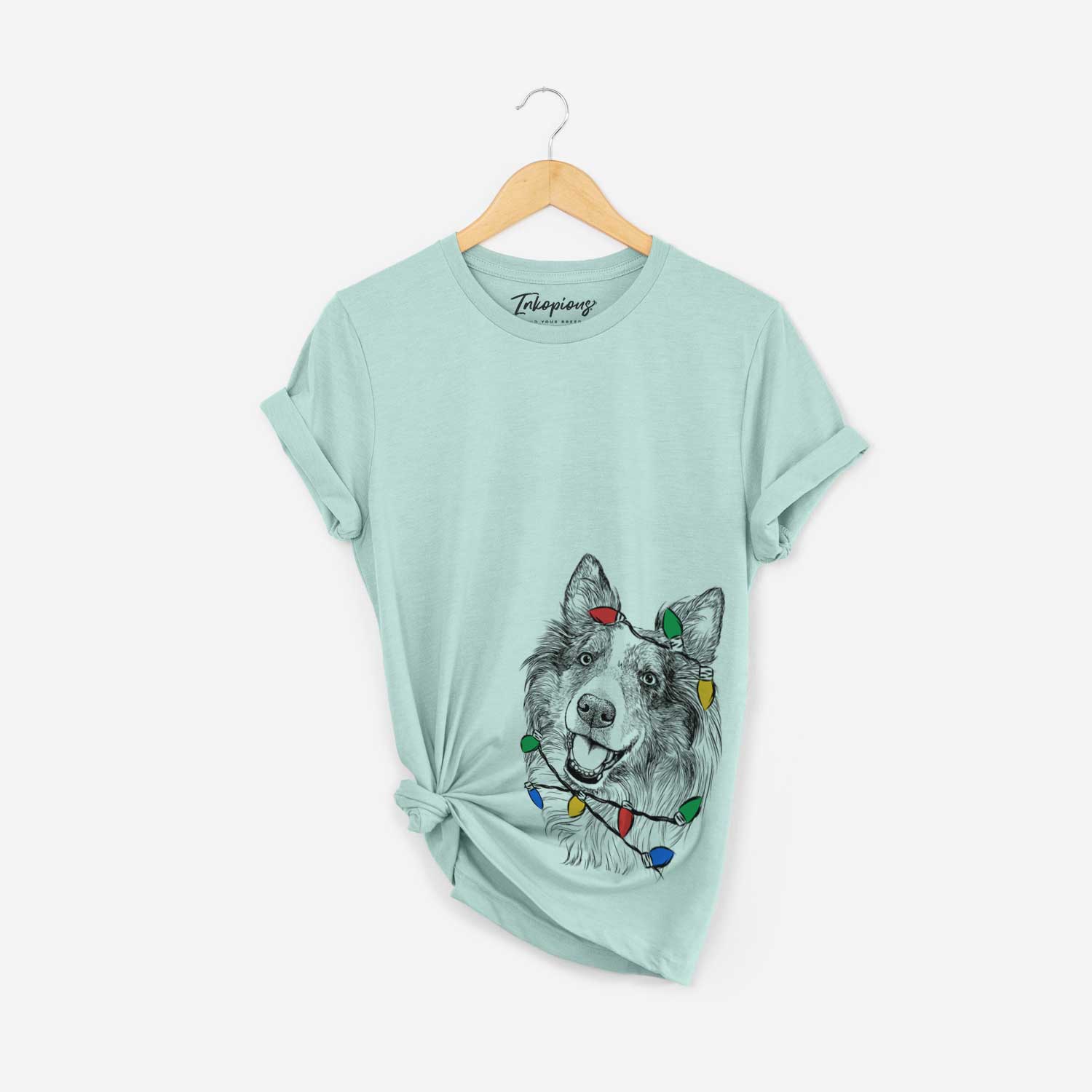 Hand-drawn sketch of Skylar the Shetland Sheepdog wrapped in Christmas lights on a Heather Sage Unisex crewneck