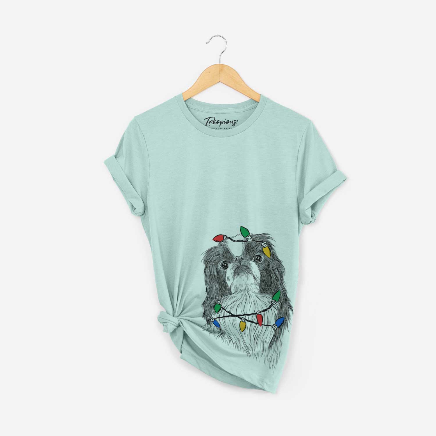 Hand-drawn sketch of Suki the Japanese Chin wrapped in Christmas lights on a Heather Sage Unisex crewneck