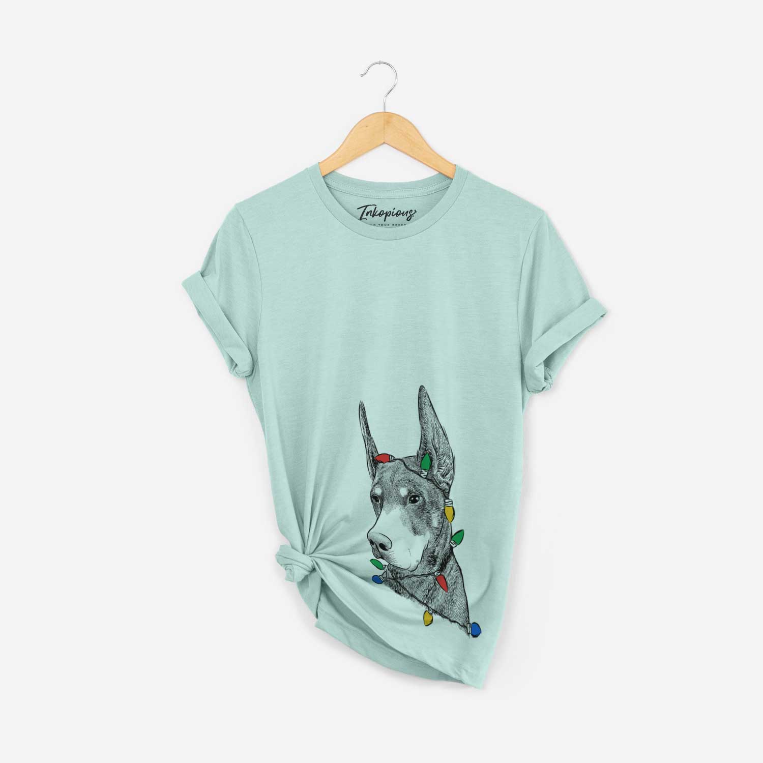 Hand-drawn sketch of Sunny the Doberman Pinscher wrapped in Christmas lights on a Heather Sage Unisex crewneck
