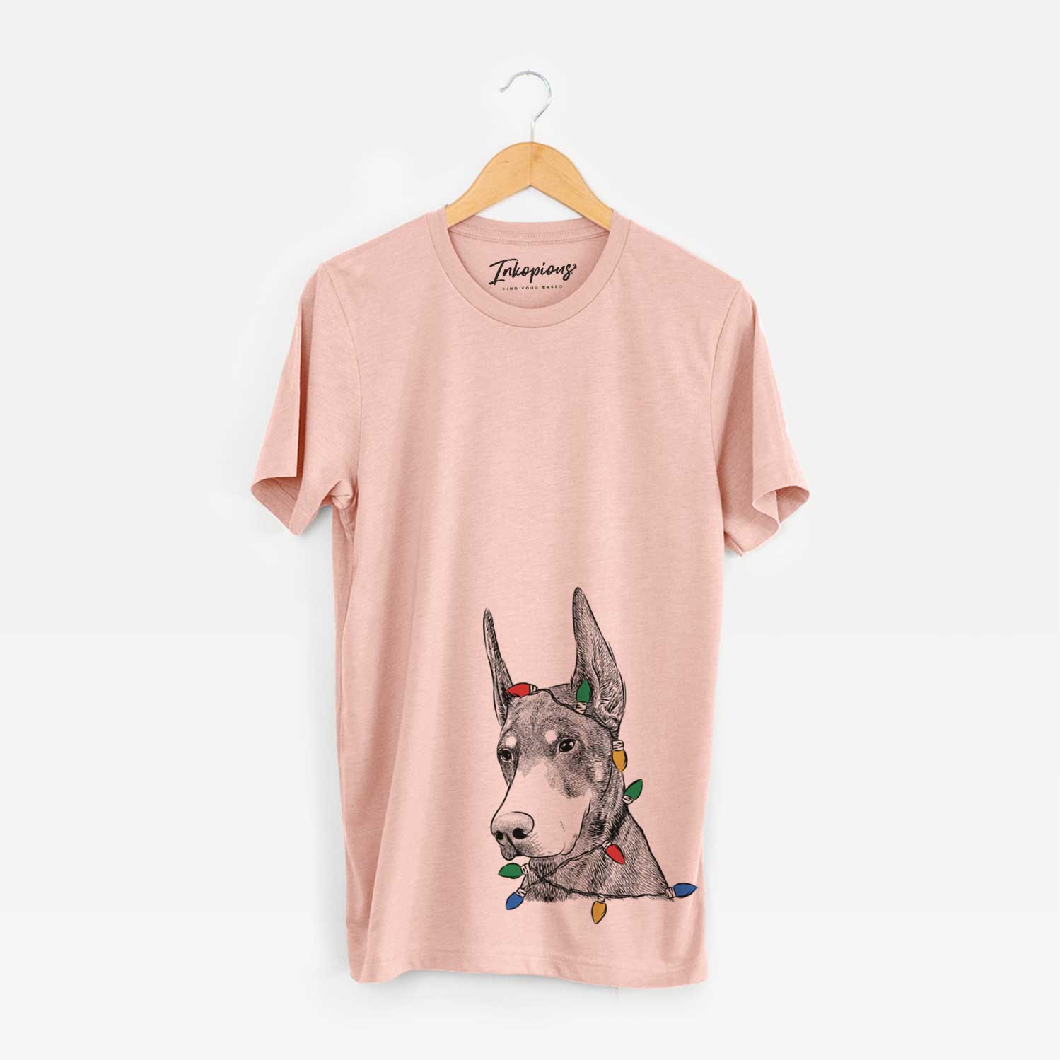 Hand-drawn sketch of Sunny the Doberman Pinscher wrapped in Christmas lights on a Peach Unisex crewneck