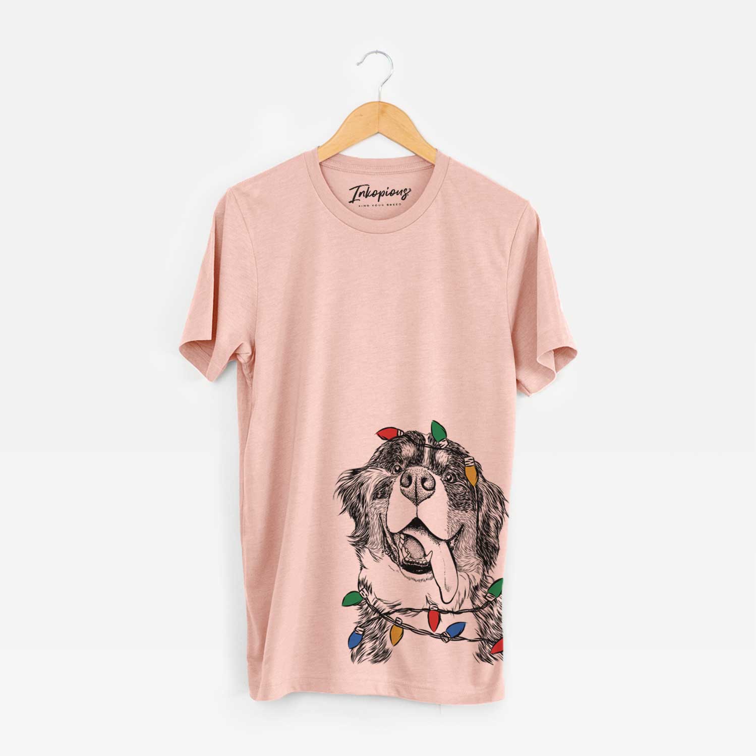 Hand-drawn sketch of Theo the Bernese Mountain Dog wrapped in Christmas lights on a Peach Unisex crewneck