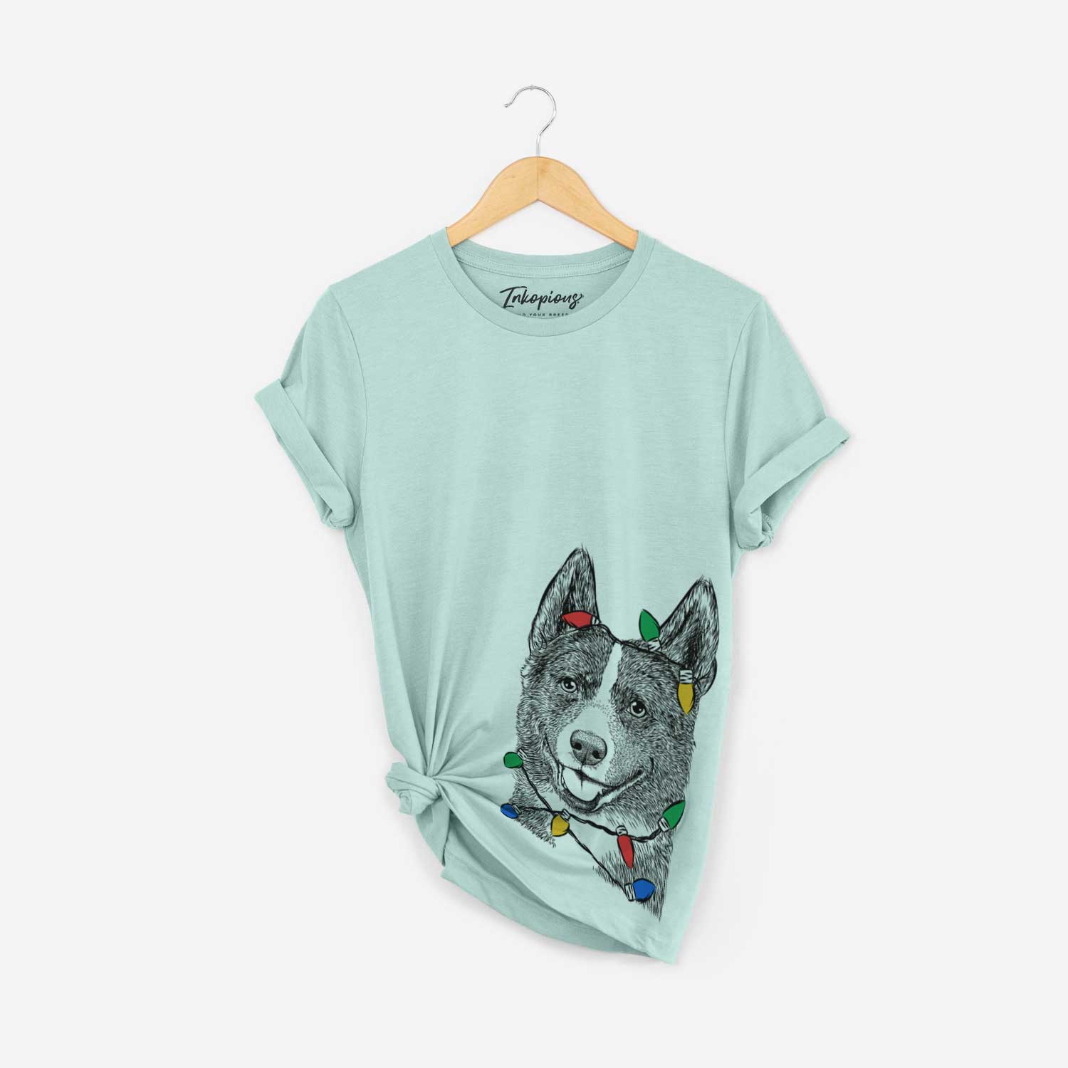 Hand-drawn sketch of Tosca the Karelian Bear Dog wrapped in Christmas lights on a Heather Sage Unisex crewneck