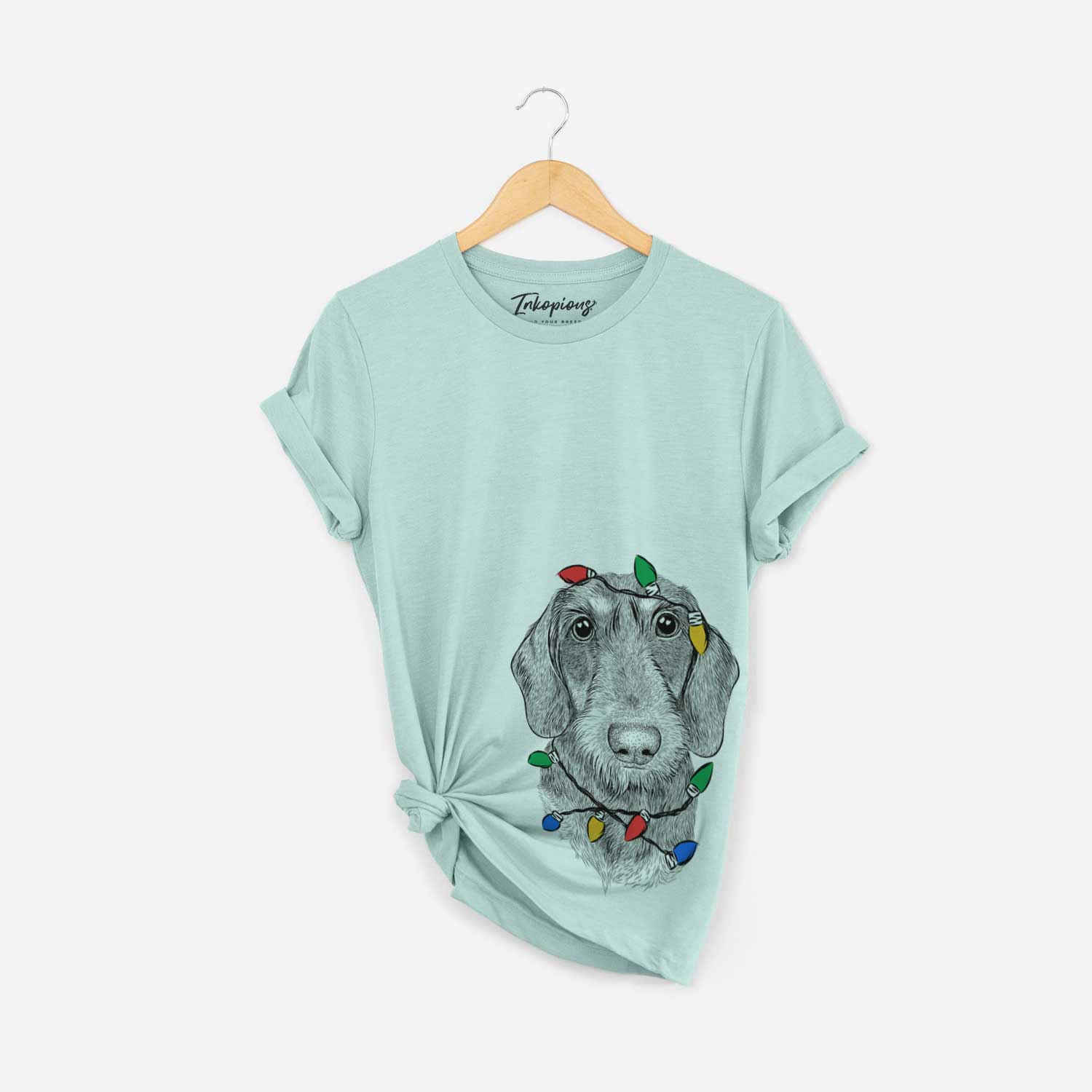 Hand-drawn sketch of Truman the Wirehaired Dachshund wrapped in Christmas lights on a Heather Sage Unisex crewneck